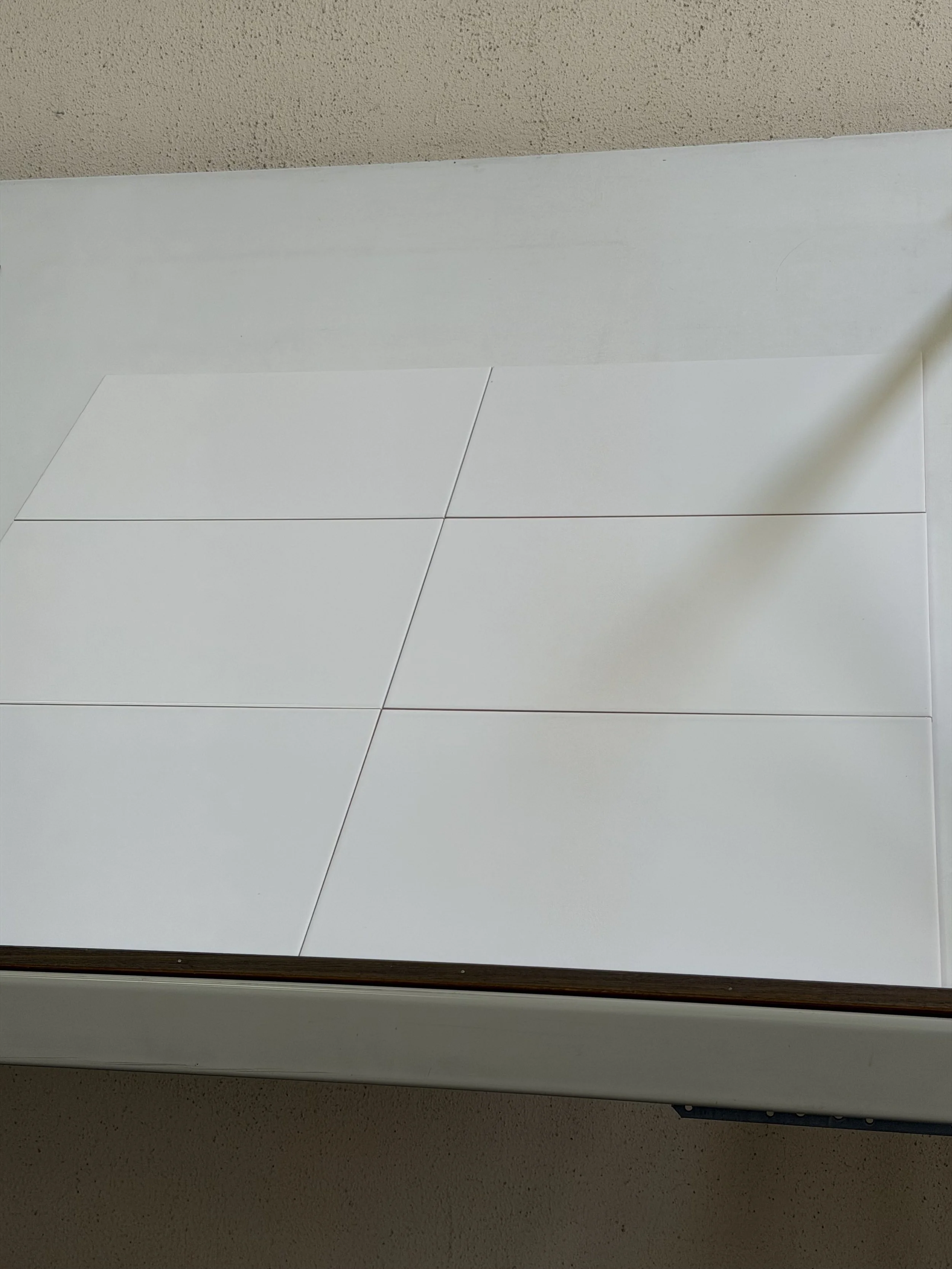 Een close-up van een wit houten of kunststof bord met omlijsting, geplaatst onder een beige geschuurde muur.