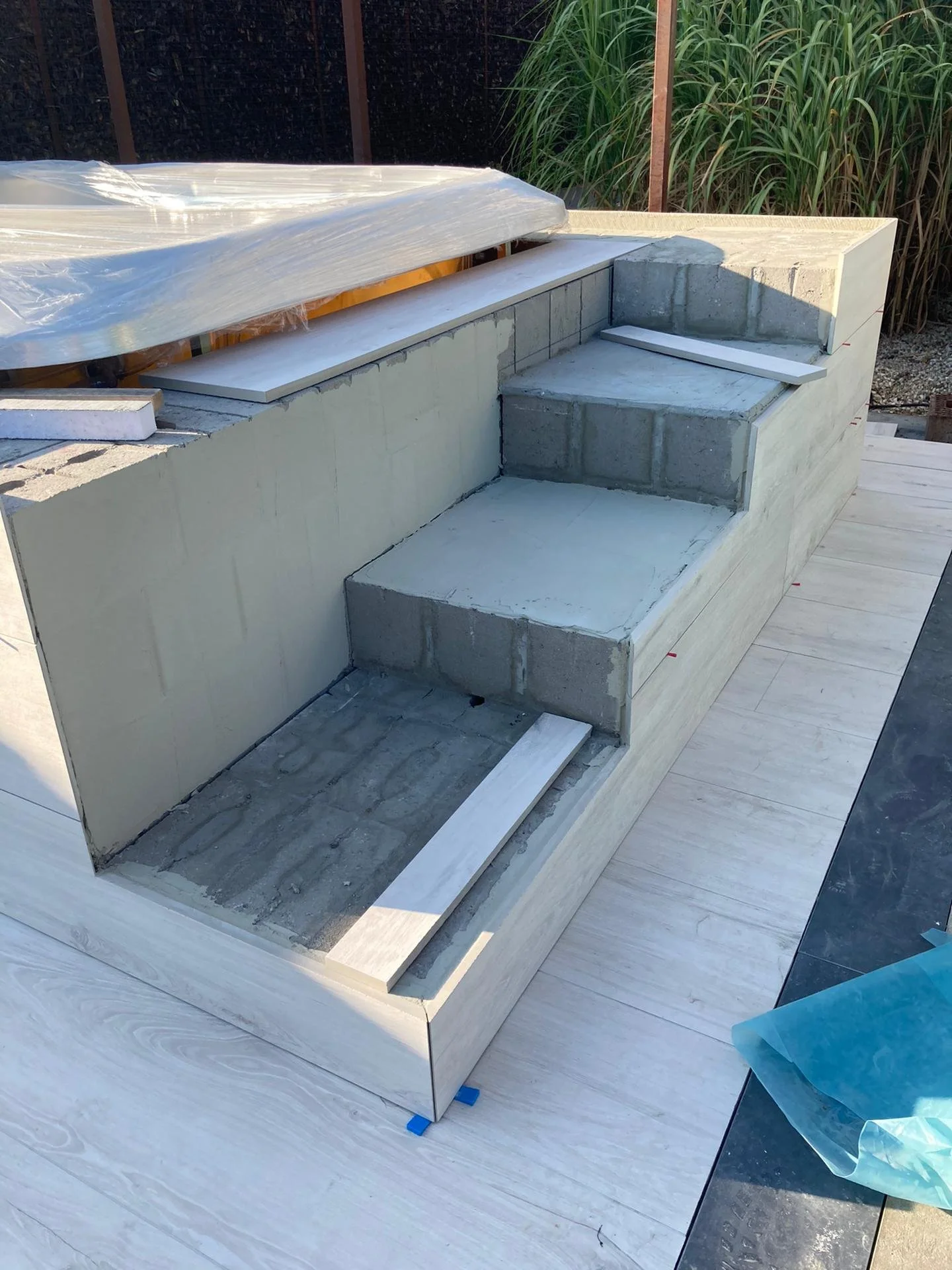 Onder constructie liggende buitentrap met betonnen treden en omringende muren, omgeven door planten, met materialen en gereedschap ernaast.