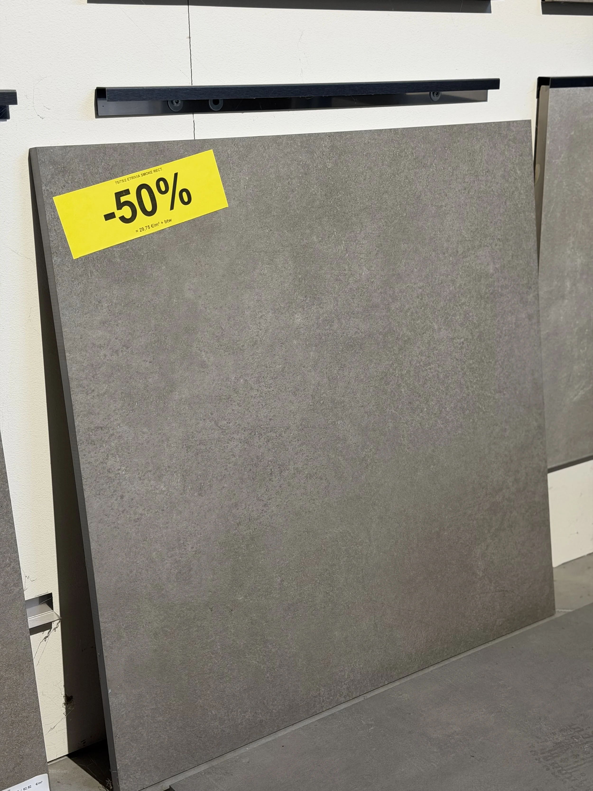 Twee grote grijze tegels of platen staan rechtop. Een ervan heeft een gele kortingssticker die 50% korting aangeeft.