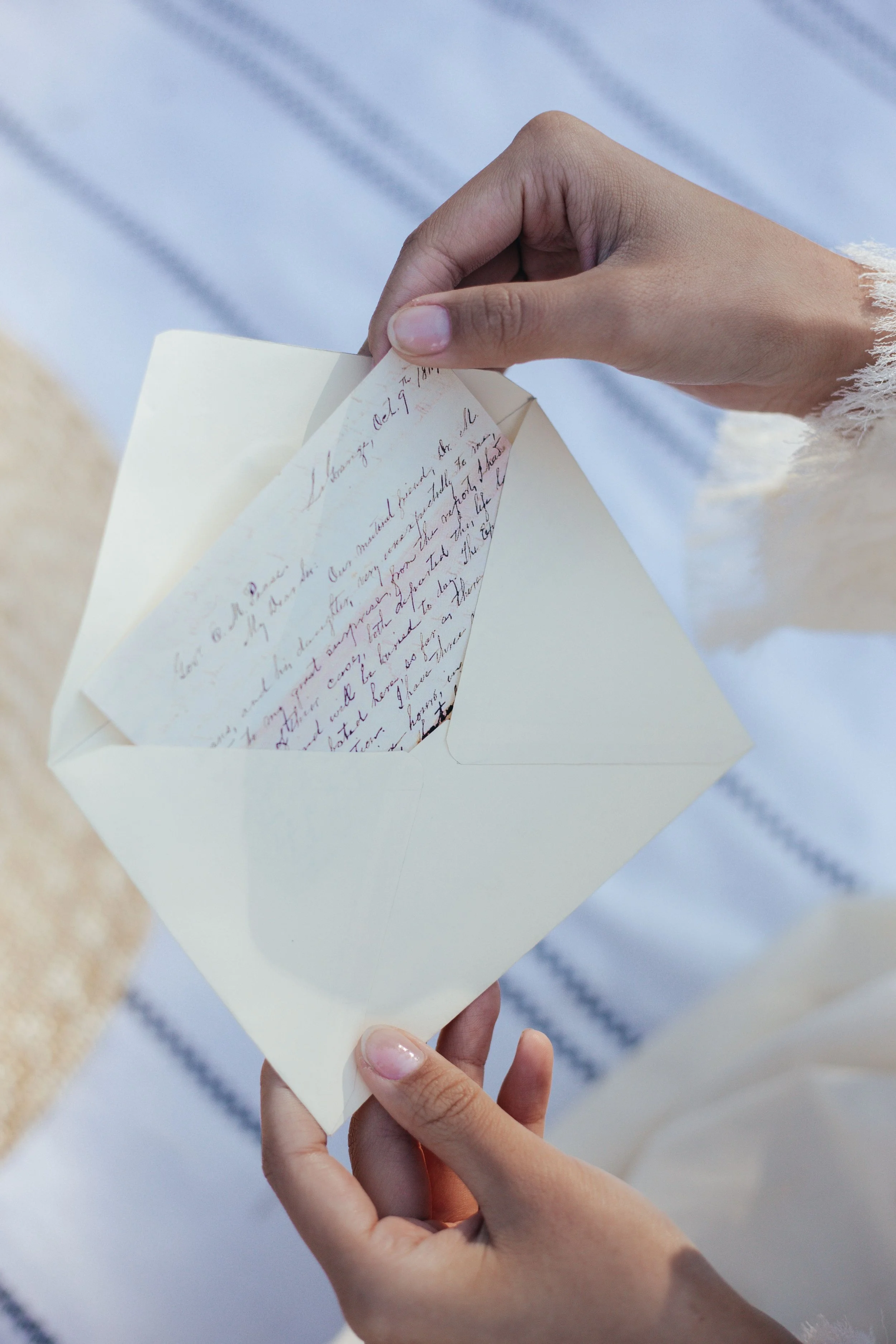 Close-up of person's hand holding an open greeting card with handwritten message inside, against outdoor background with snow and a striped surface.