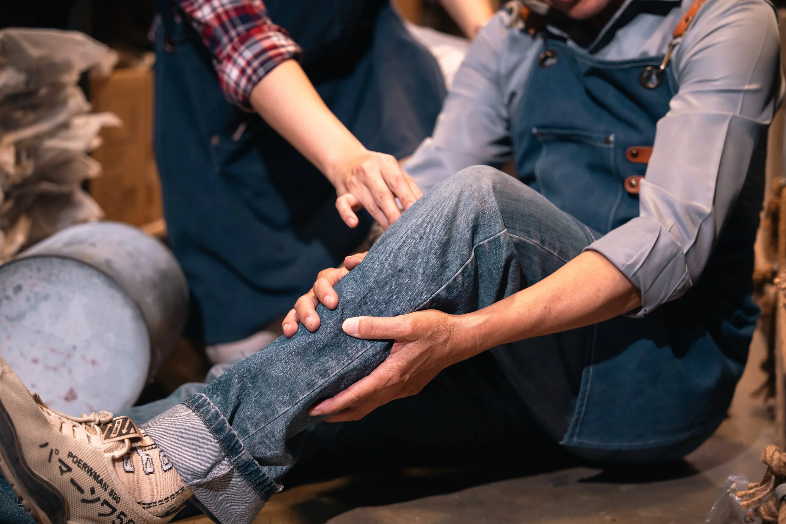 Person holding a bent knee in pain while receiving assistance from another person