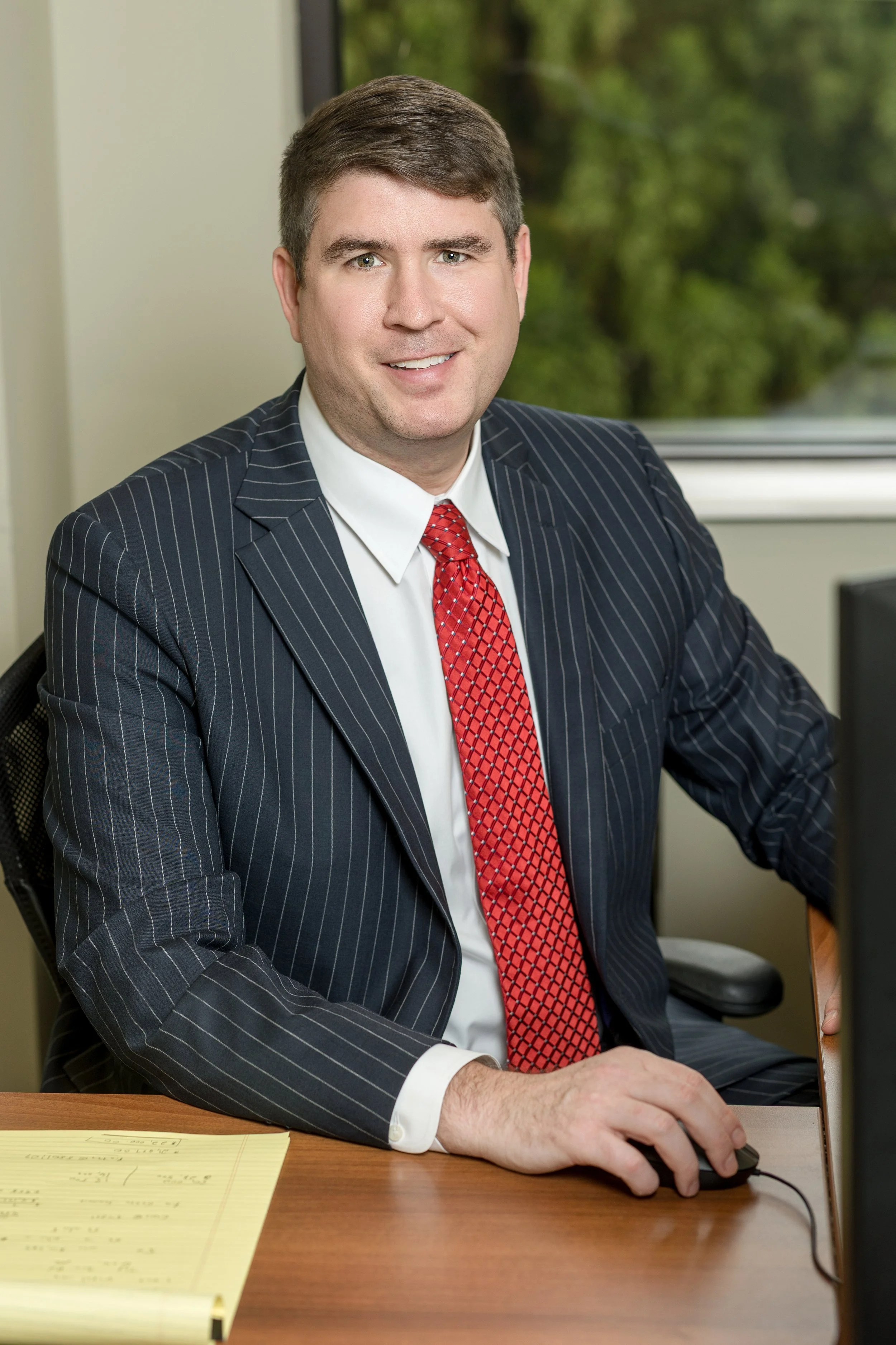 Smiling businessman in a pinstripe suit and red tie working at a desk with a computer mouse
