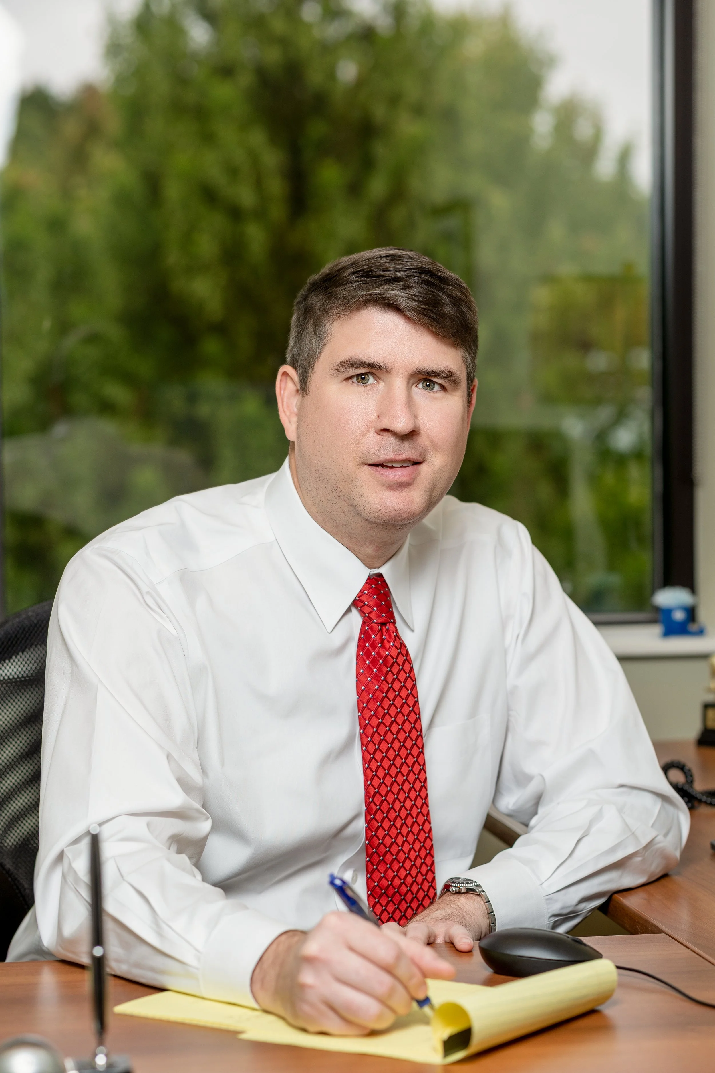 Man in a white shirt and red tie writing at an office desk