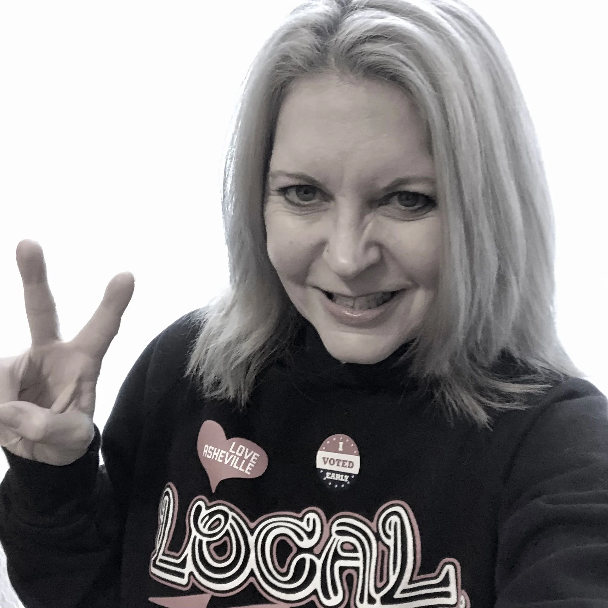 Claudette Silver holding up a peace sign with her fingers and wearing a "Love Asheville, Go Local" shirt