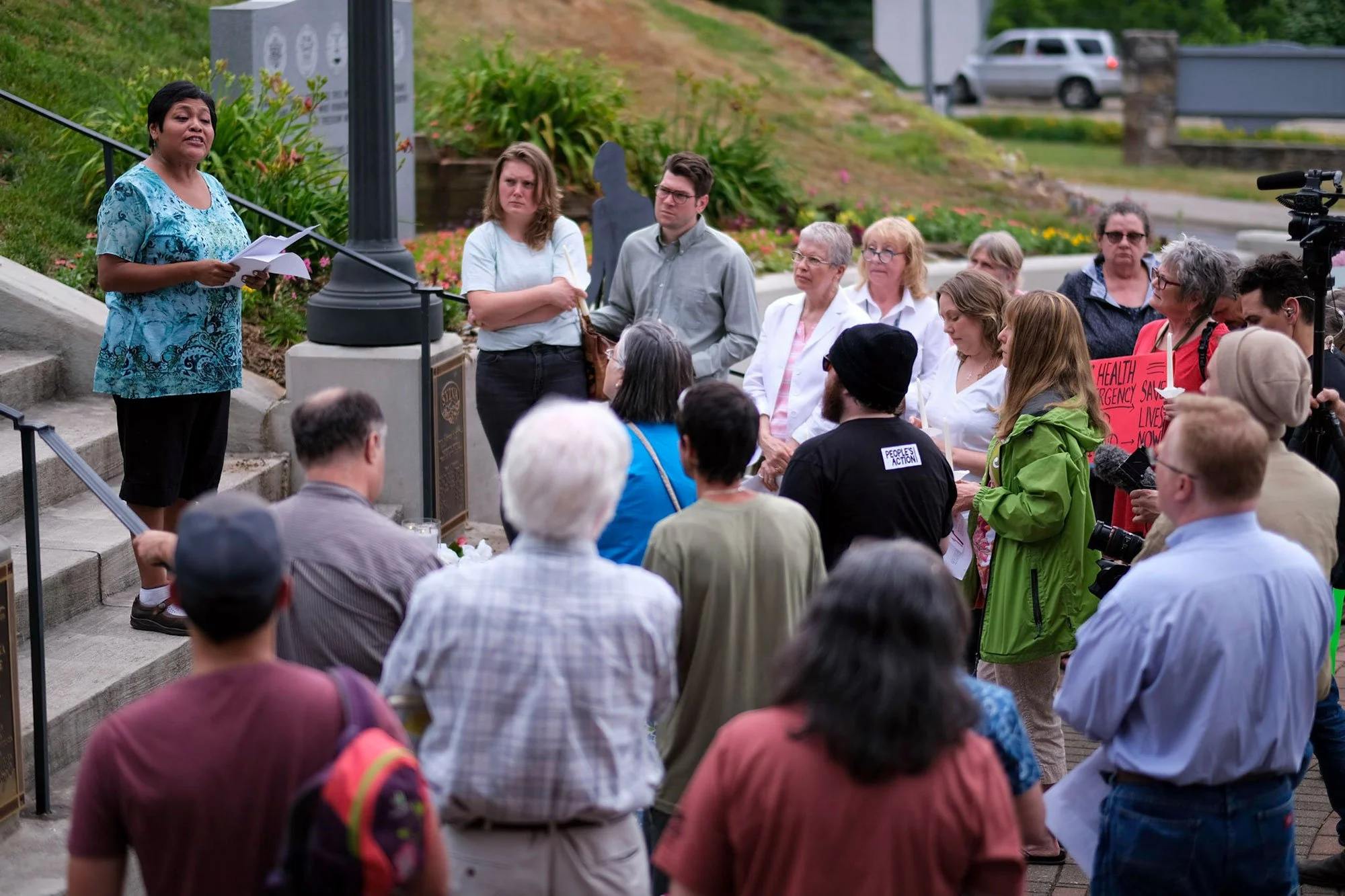 Group of people standing around a staircase outside while a woman stands on the steps talking