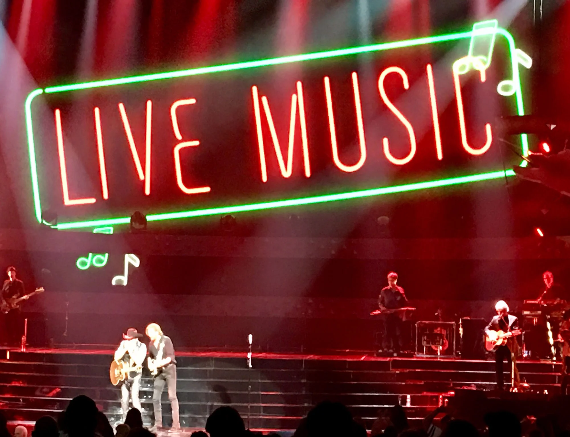 Stage lit with red lights with musicians on it and a large neon sign reading "live music" above them.