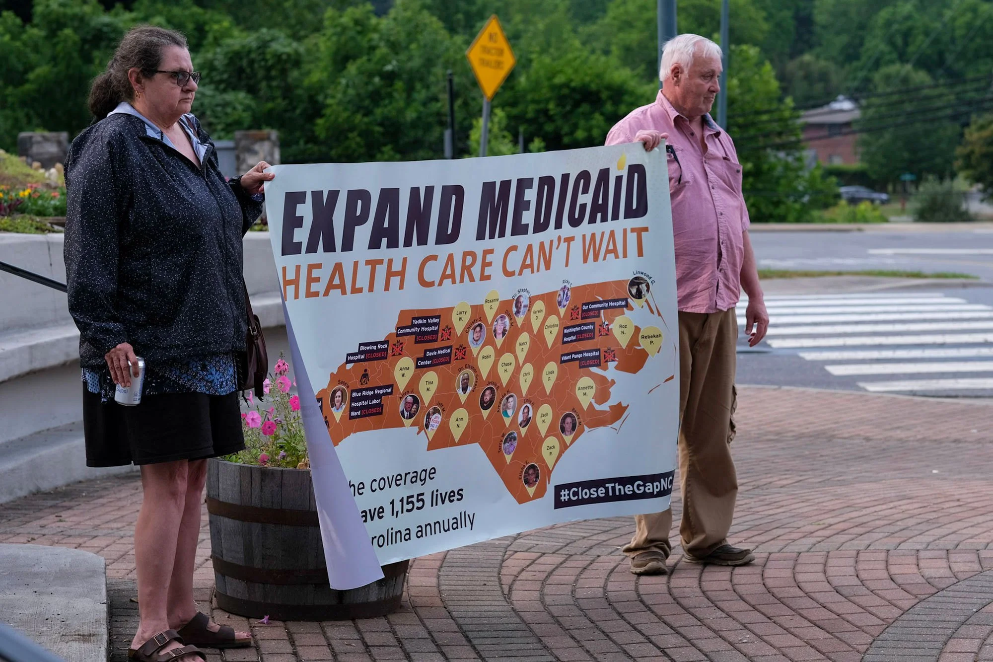 A man and a woman each holding the corner of a banner that says "expand Medicaid, health care can't wait" with a map of the U.S.
