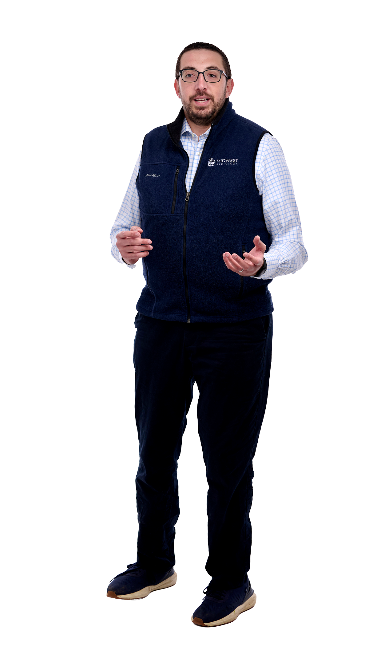 A man wearing glasses and a Midwest Neurology vest, standing and speaking, with a light checkered shirt, dark pants, and sneakers.