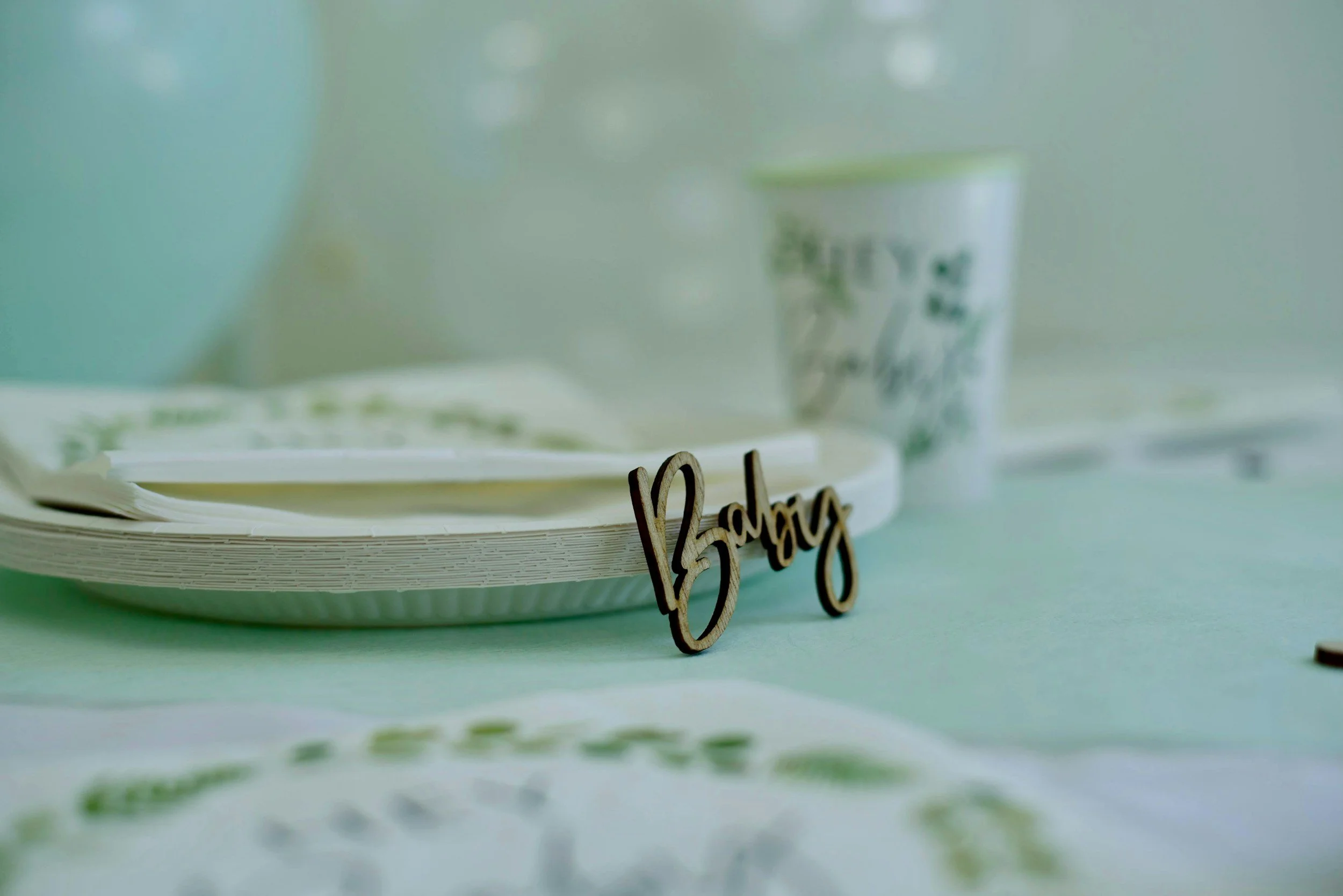 Close-up of a white plate with a white cup in the background and the word 'family' in cursive wood letters on the plate, against a light background.