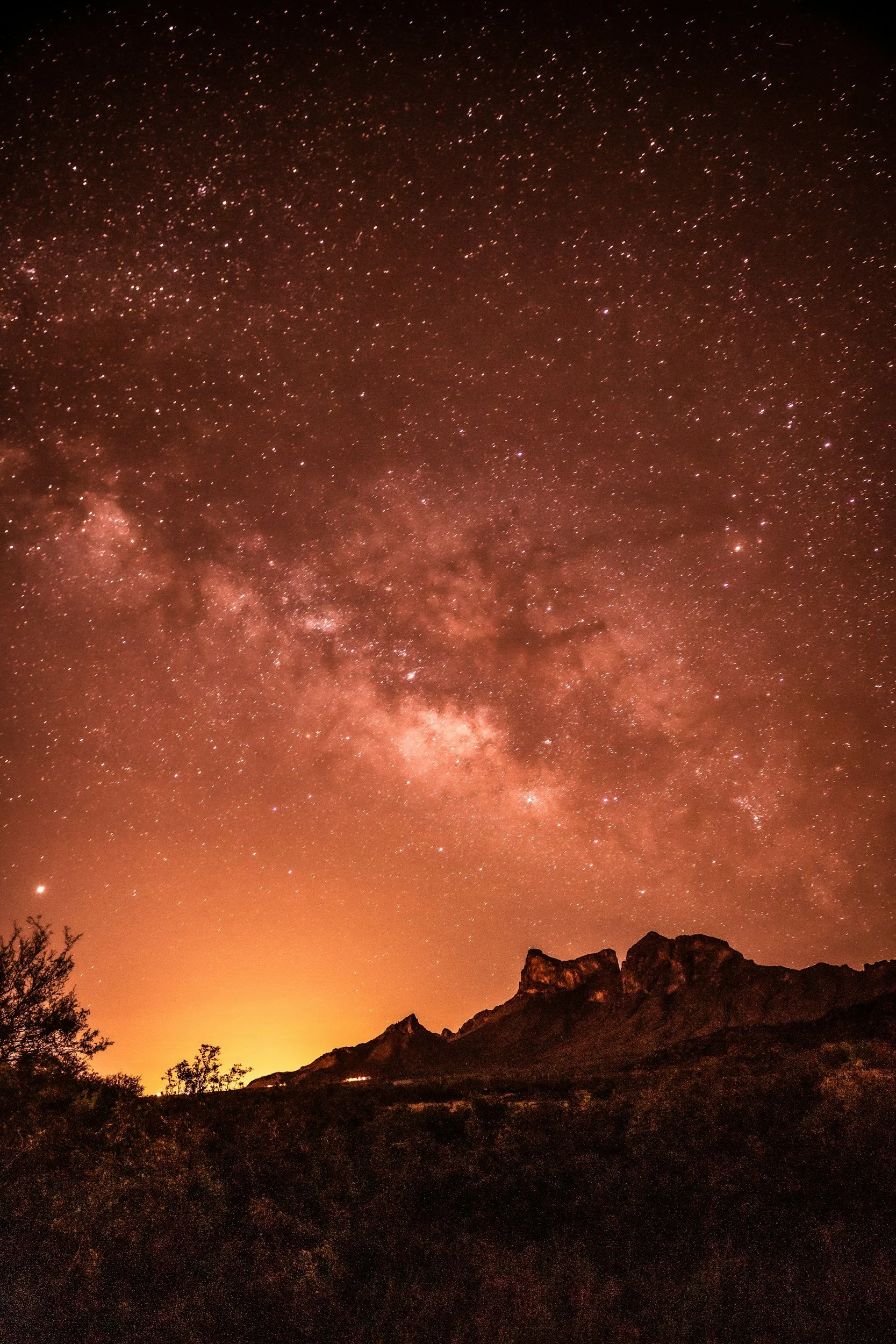 Night sky filled with stars above mountain landscape at dusk, with silhouettes of trees and mountain peaks in the foreground.
