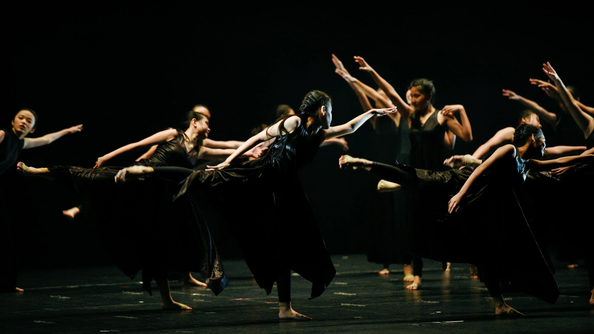 Group of dancers in black costumes performing on stage with synchronized movements.