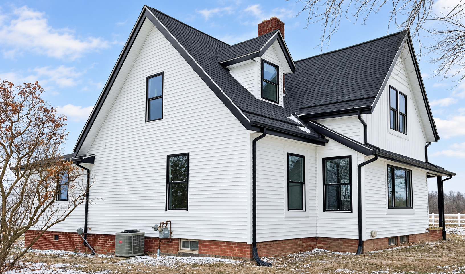 A two-story white house with black trim and a dark gray roof, with snow on the ground and some bare trees nearby.