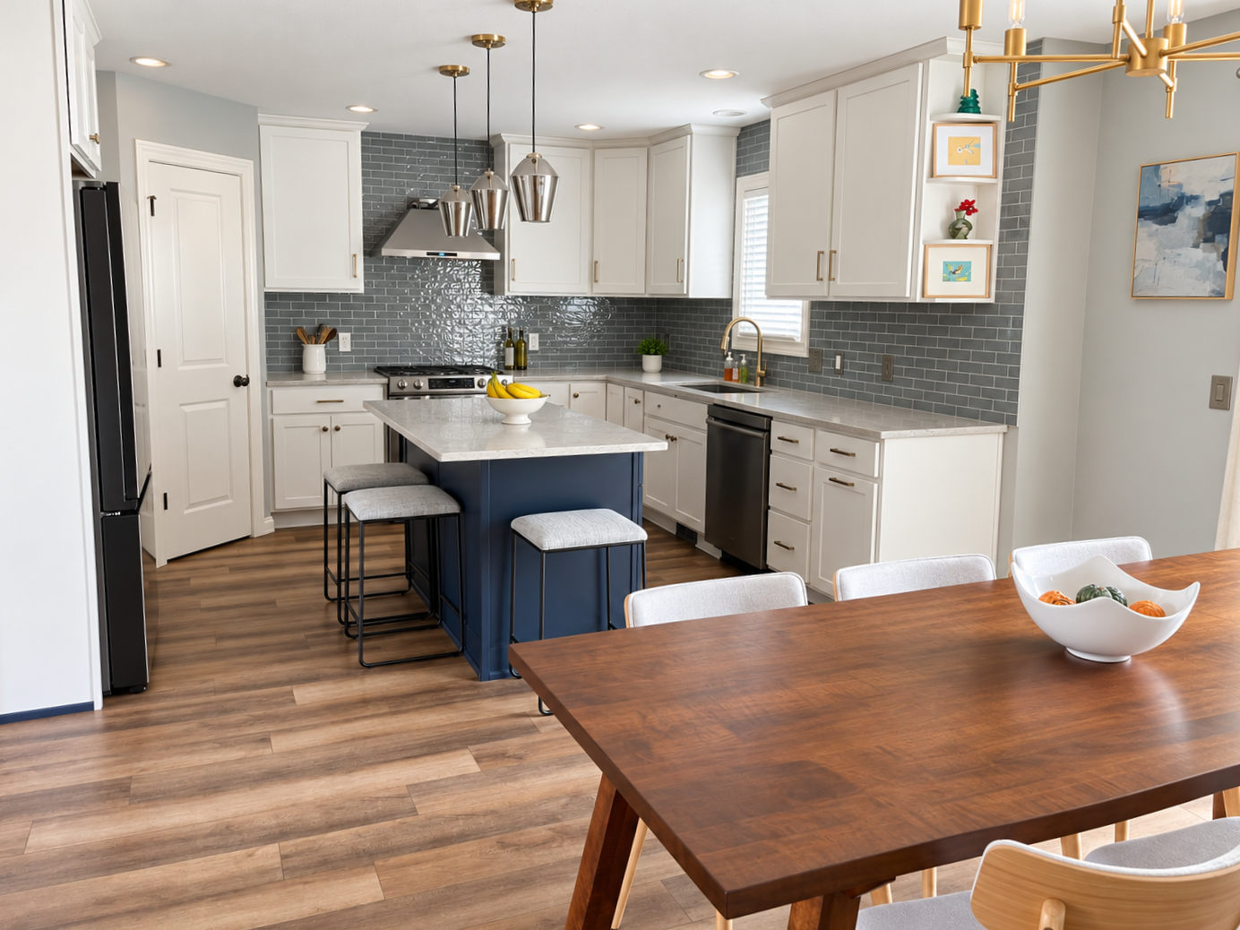 Modern kitchen with white cabinets, gray subway tile backsplash, and a navy blue island. Wooden dining table with white and light wood chairs, and a bowl of decorative fruit.