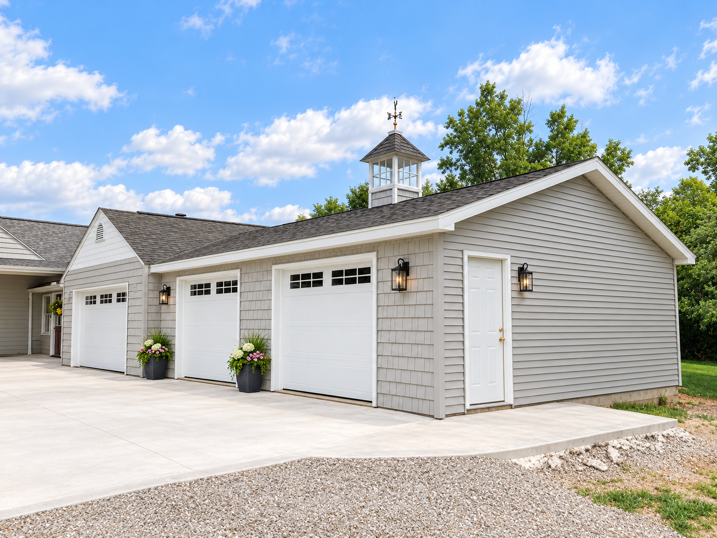 A detached garage with three white doors, potted plants in front, and exterior wall-mounted lights, under a partly cloudy blue sky.