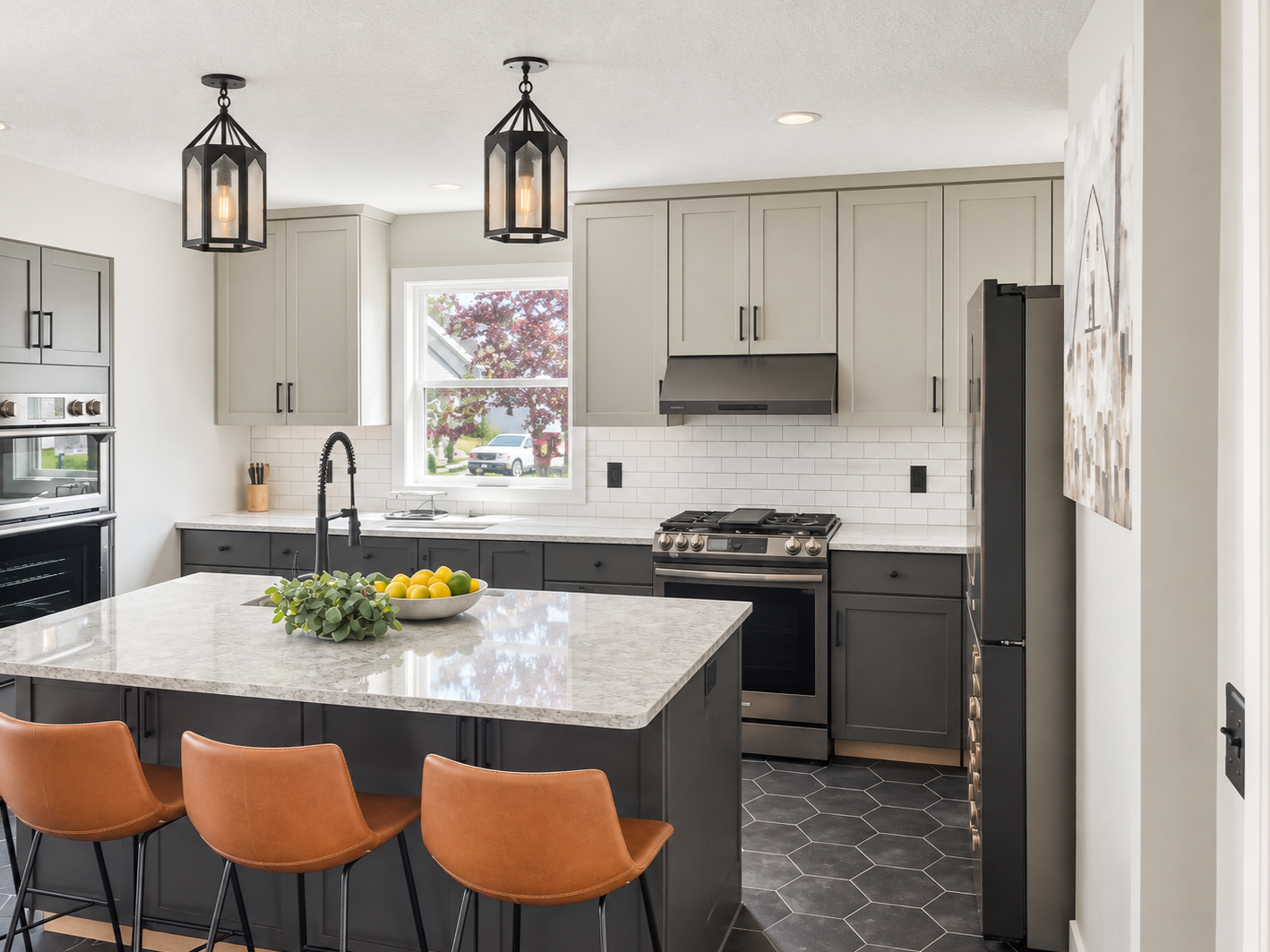 Modern kitchen with white cabinets, black accents, gray lower cabinets, white subway tile backsplash, and black honeycomb tile flooring. Features a marble kitchen island with a bowl of lemons and limes, pendant lights, a black faucet, and stainless steel appliances, with a window showing trees and parked cars outside.