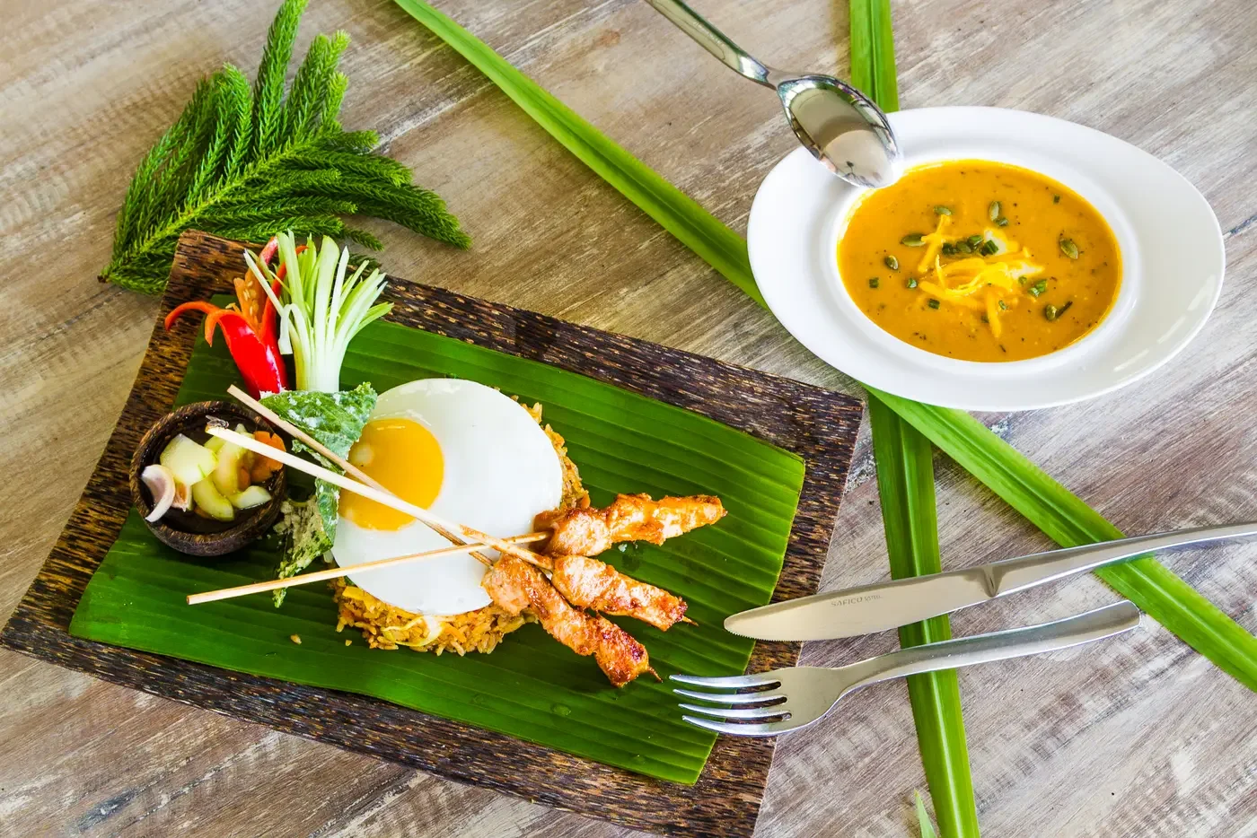 Top-down food photography of traditional Indonesian Nasi Goreng with fried egg and satay skewers alongside soup at The Griya Villas & Spa in Amed, Bali, photographed by Seña Studio.