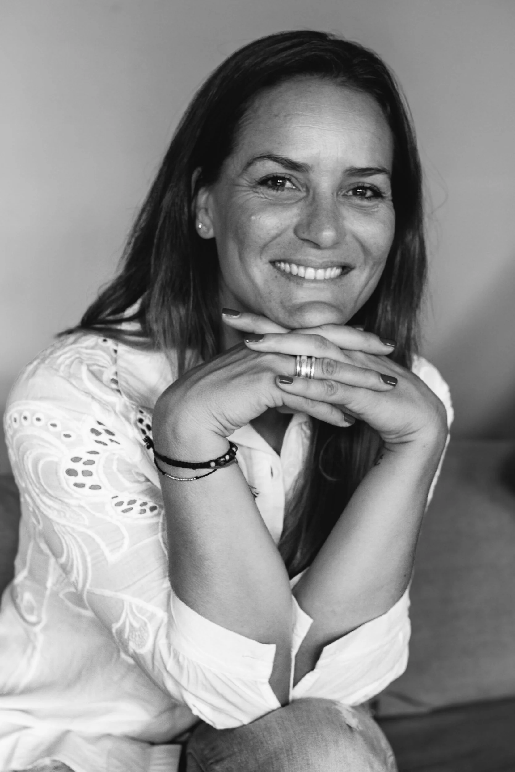 Black and white close-up portrait of a cheerful woman smiling with her hands clasped under her chin.