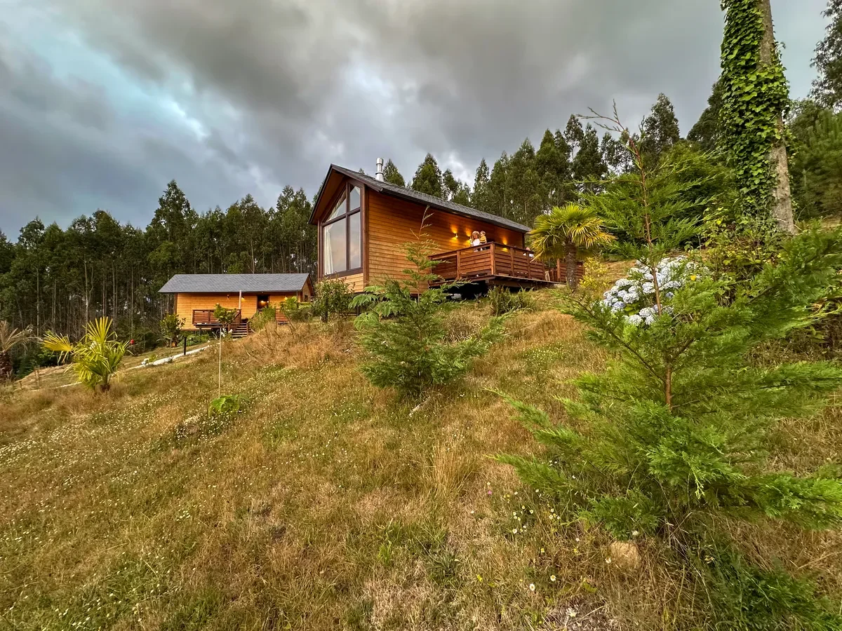 Exterior view of luxury wooden cabins at Hara de Bordo, nestled on a hillside surrounded by lush greenery in Galicia, photographed by Seña Studio.