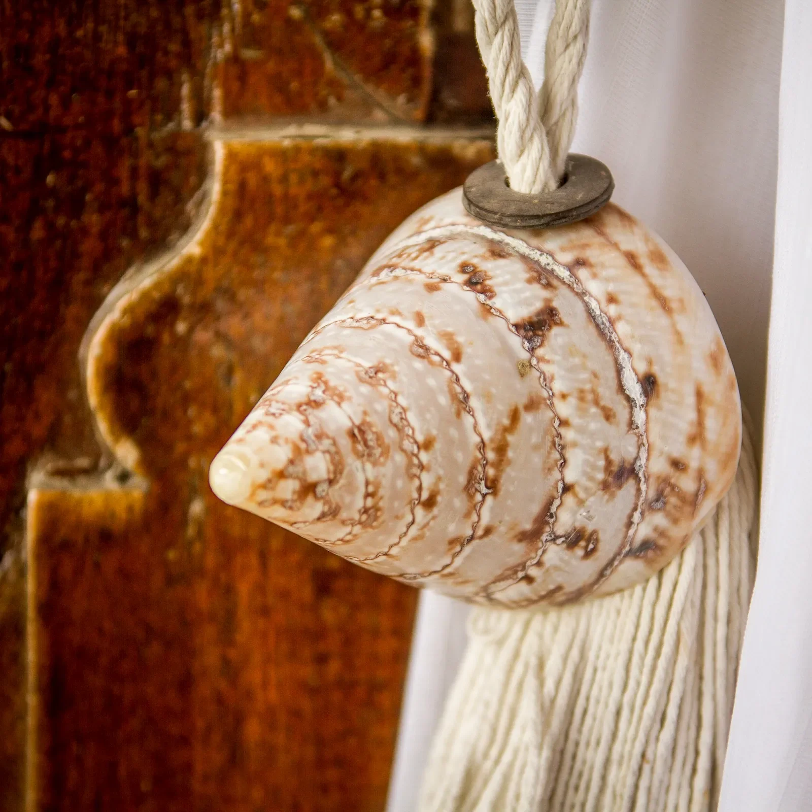Macro photograph of a cone seashell and rope tassel used as a decorative curtain tieback at Aquamarine Beach Villas in Amed, Bali, photographed by Seña Studio.