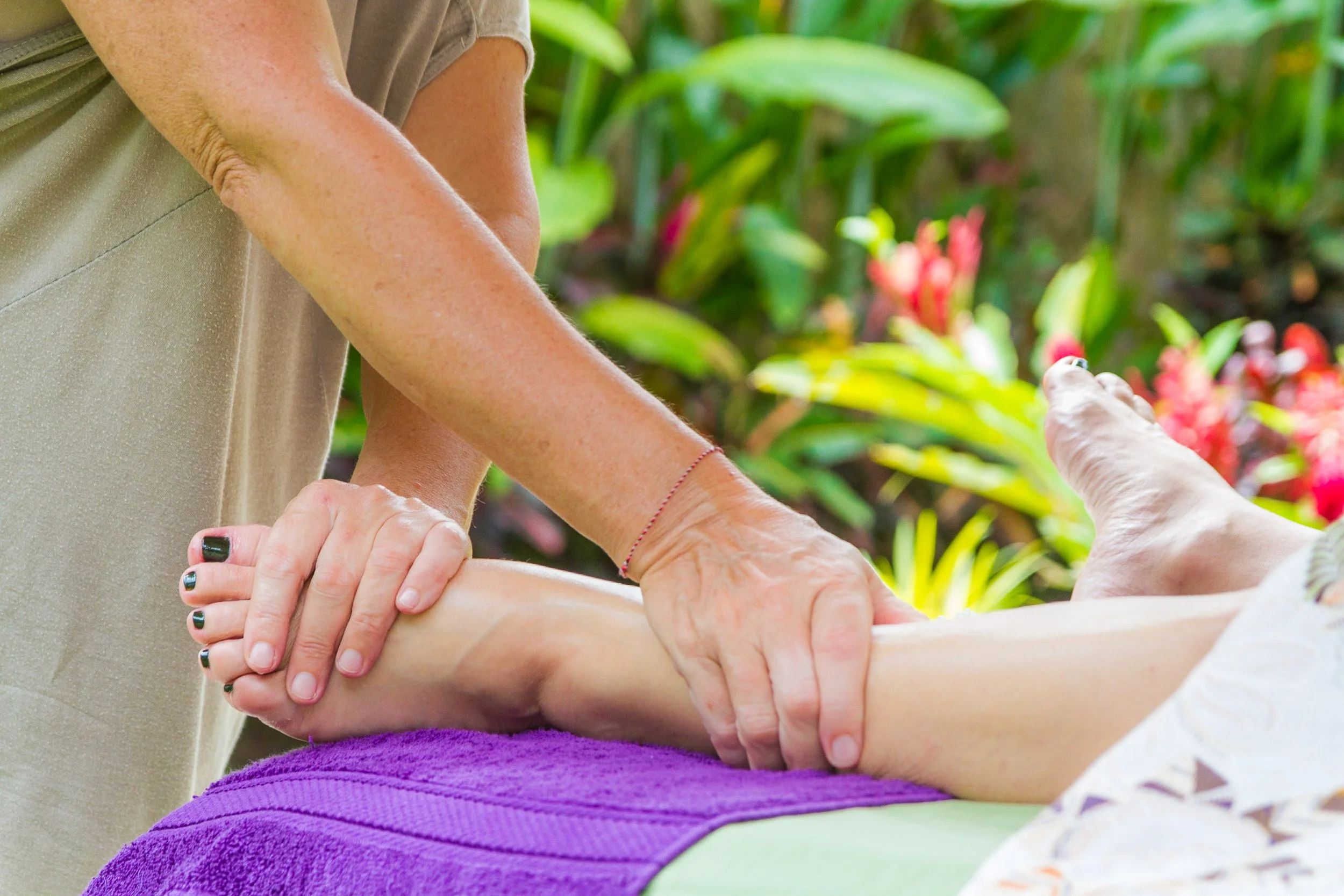 Detailed shot of a practitioner's hands applying gentle acupressure pressure to a client's foot during an outdoor wellness session, photographed by Seña Studio.