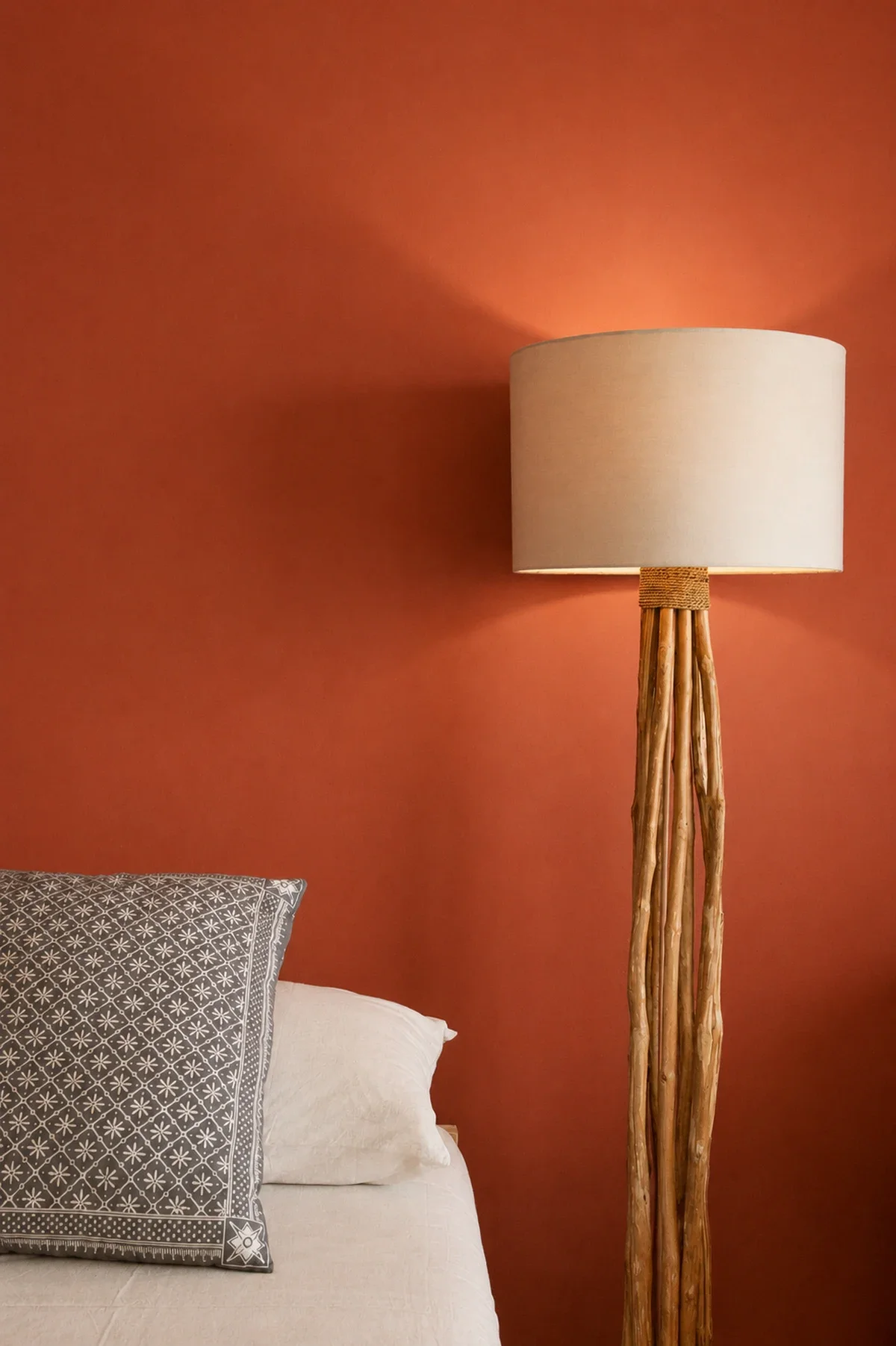 Interior detail of a wooden floor lamp standing beside a bed against a warm terracotta accent wall at Villa Aquamarine in Amed, Bali, photographed by Seña Studio.