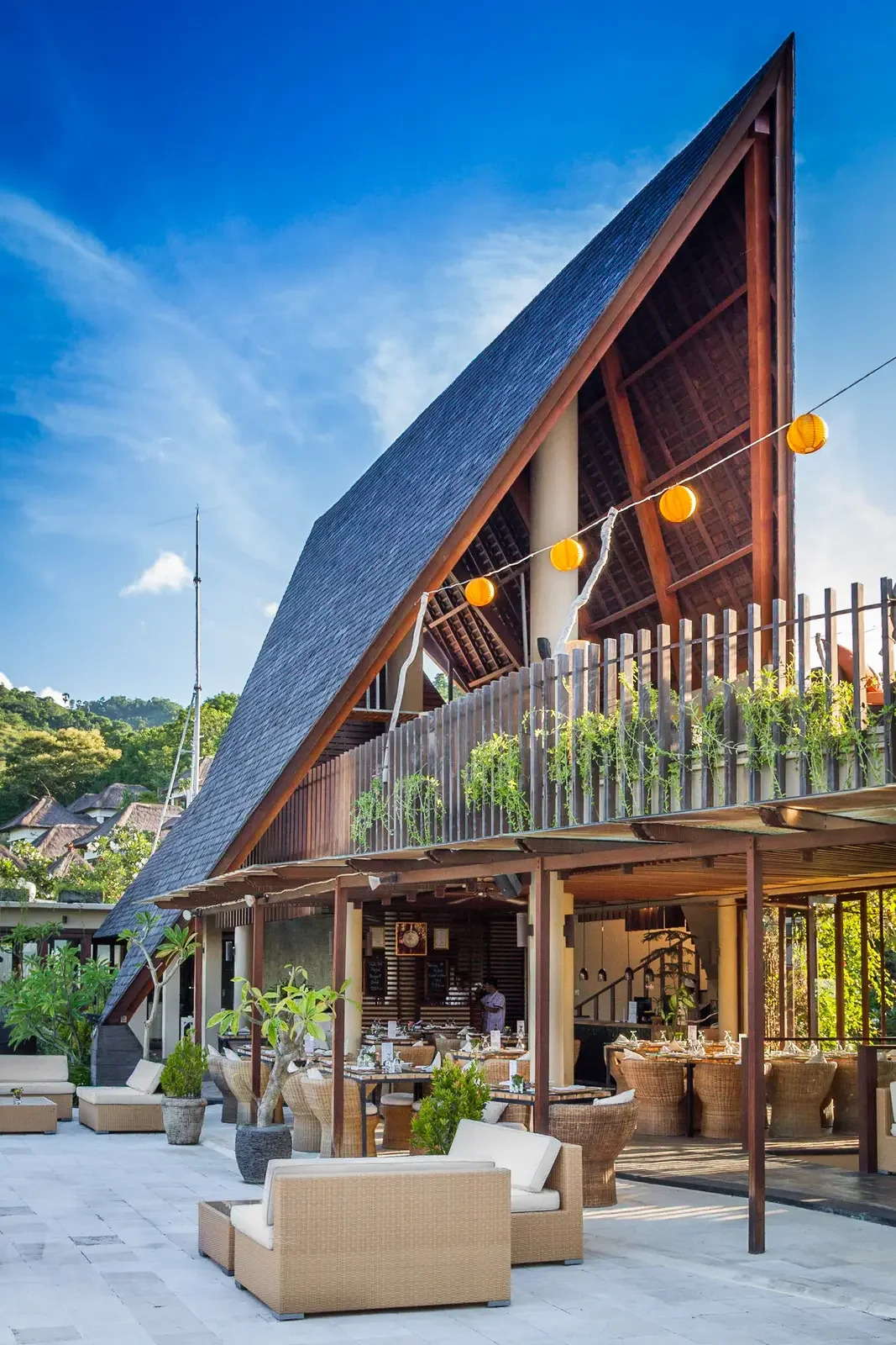 Striking architectural view of an open-air resort restaurant with a high thatched roof and outdoor terrace seating at The Griya Villas & Spa in Amed, Bali, photographed by Seña Studio.