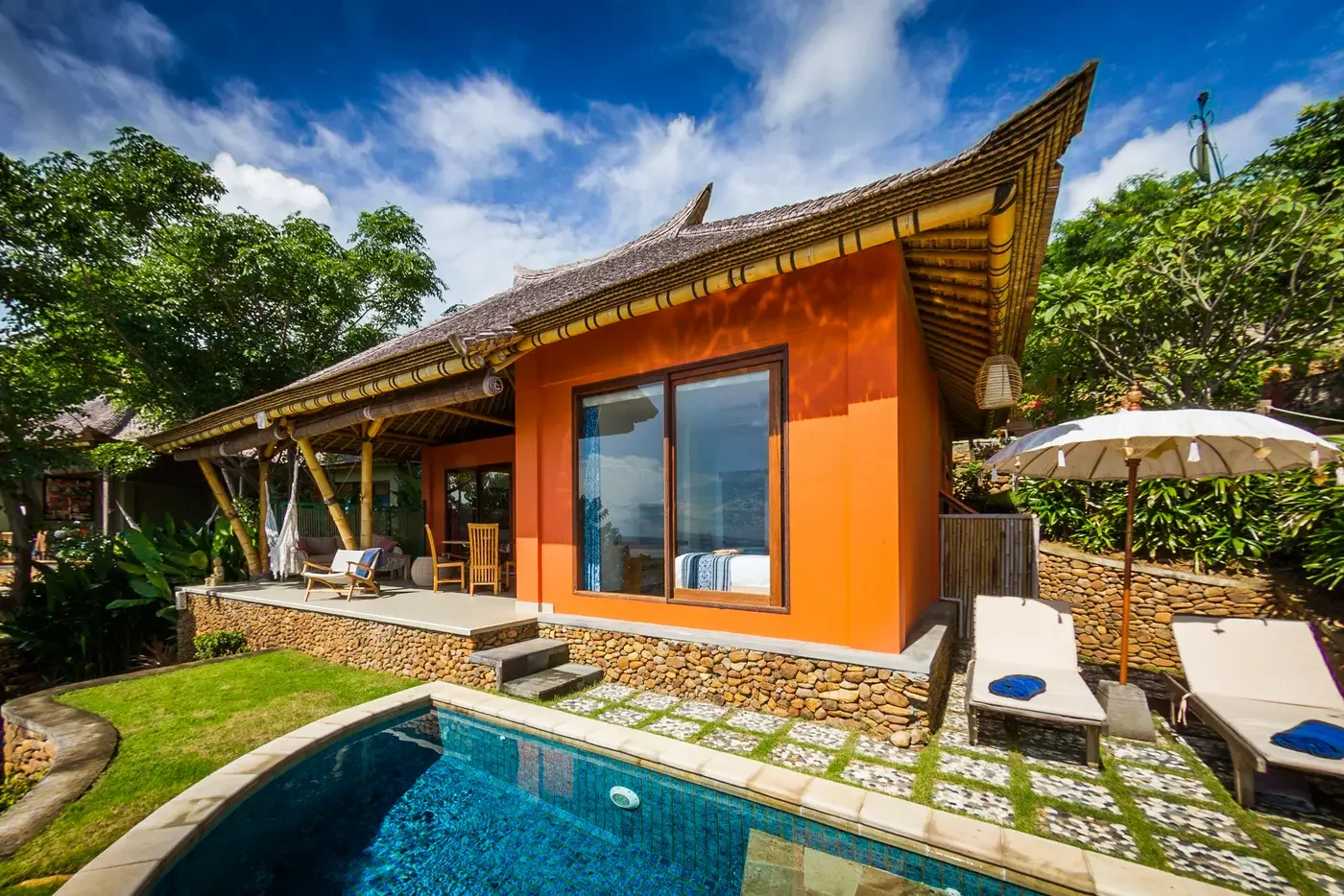 Bright orange villa exterior with a private plunge pool, sun loungers, and tropical thatch roofing at Villa Aquamarine in Amed, Bali, photographed by Seña Studio.