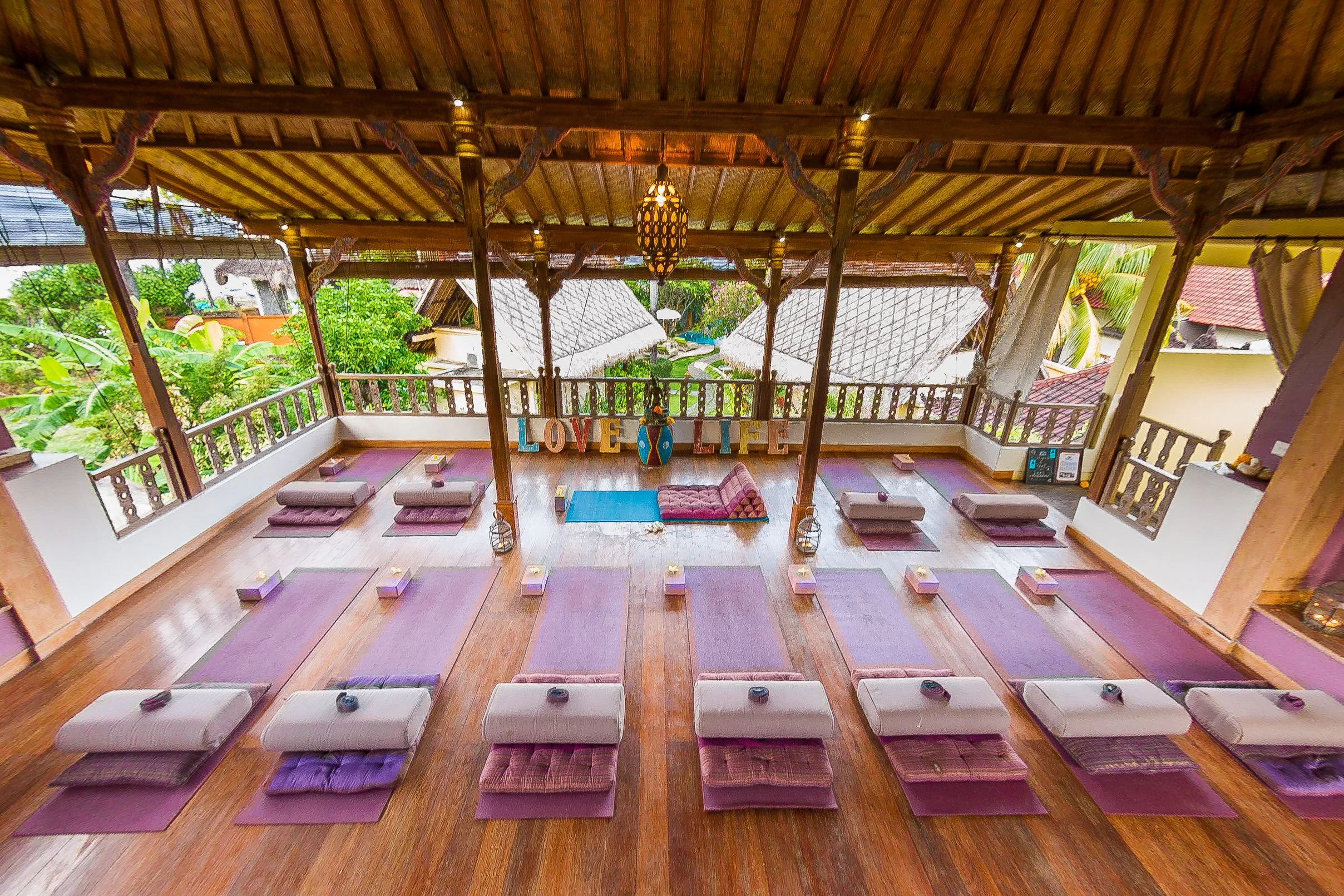 High-angle perspective of purple yoga mats and matching foam blocks neatly laid out on polished hardwood floors, each decorated with fresh frangipani flowers, photographed by Seña Studio.