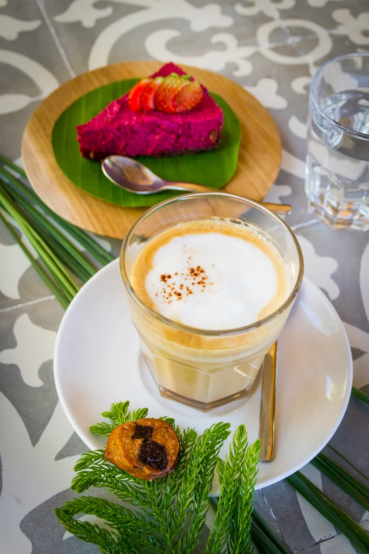 Frothy café latte served alongside a slice of vibrant pink strawberry cheesecake on a patterned cafe table, photographed by Seña Studio.
