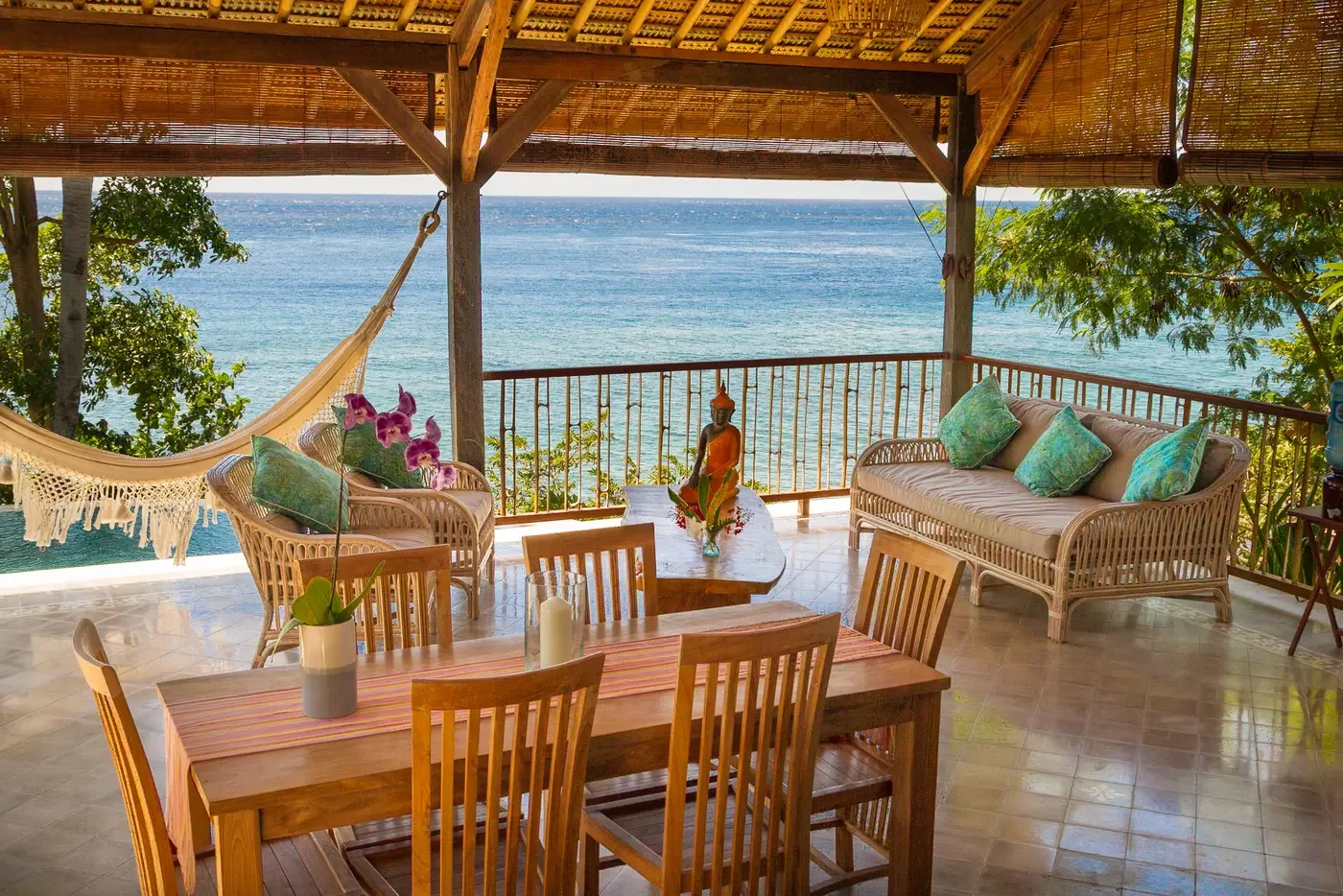 Open-air covered terrace with a dining table, wicker lounge seating, and a hammock overlooking the ocean at Villa Aquamarine in Amed, Bali, photographed by Seña Studio.