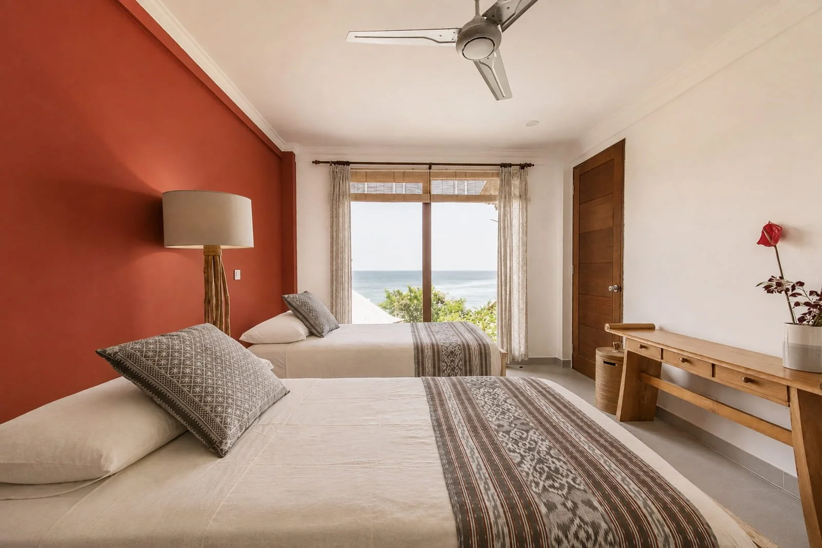 Bright bedroom suite featuring two beds, terracotta accent wall, and a large window overlooking the ocean at Villa Aquamarine in Amed, Bali, photographed by Seña Studio.