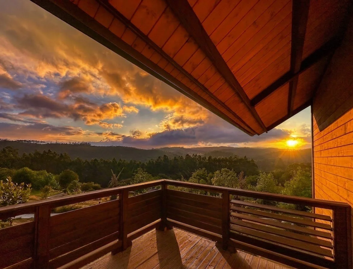 Luxury wooden cabin balcony with a panoramic golden hour sunset view over forested hills in Galicia, photographed by Sena Studio.