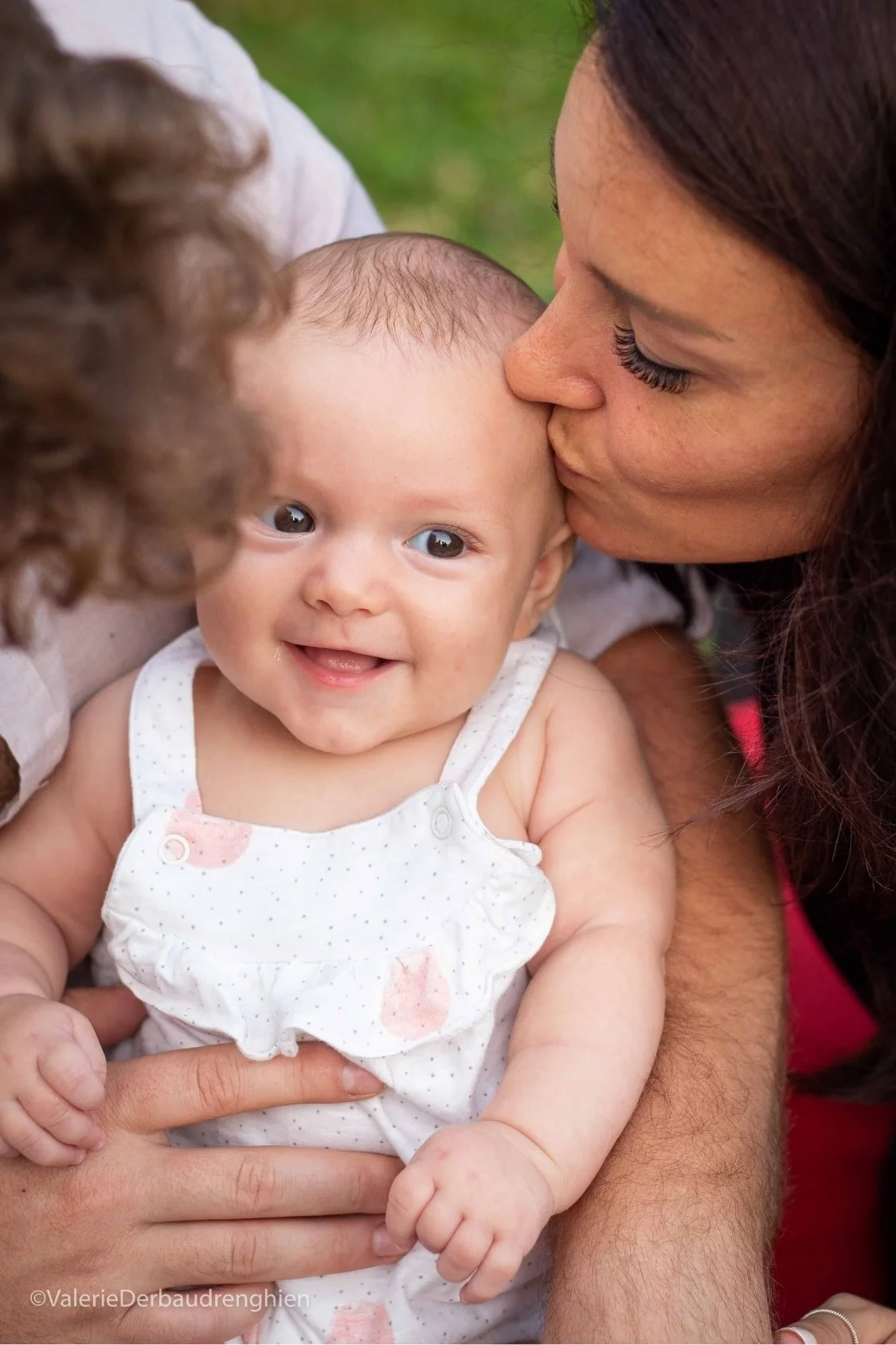 Mother kisses her smiling baby’s forehead, a tender moment from a natural light family photo session