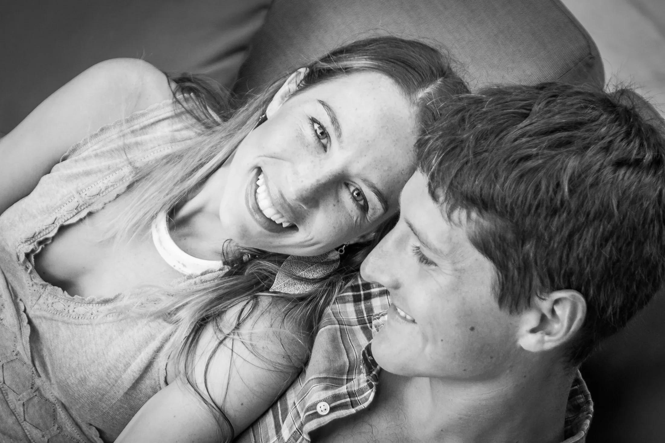 Intimate black-and-white close-up portrait of a smiling woman resting against a man's shoulder as he looks at her warmly, photographed by Seña Studio. Photo taken at The Griya Villas & Spa, Amed, Bali.