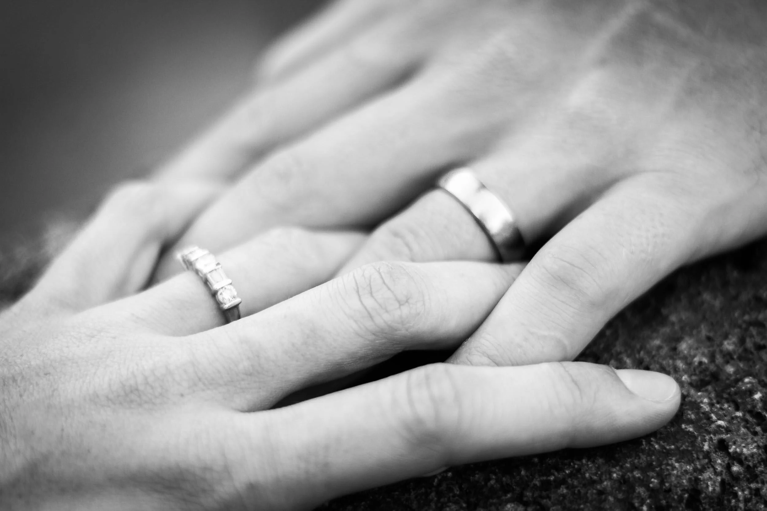 Black-and-white macro portrait of a couple holding hands, highlighting a delicate diamond band and a classic wedding ring, photographed by Seña Studio.