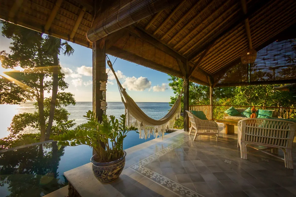 Traditional Balinese wooden gazebo with a woven hammock nestled in lush tropical gardens at Aquamarine Beach Villas, Bali, photographed by Seña Studio.