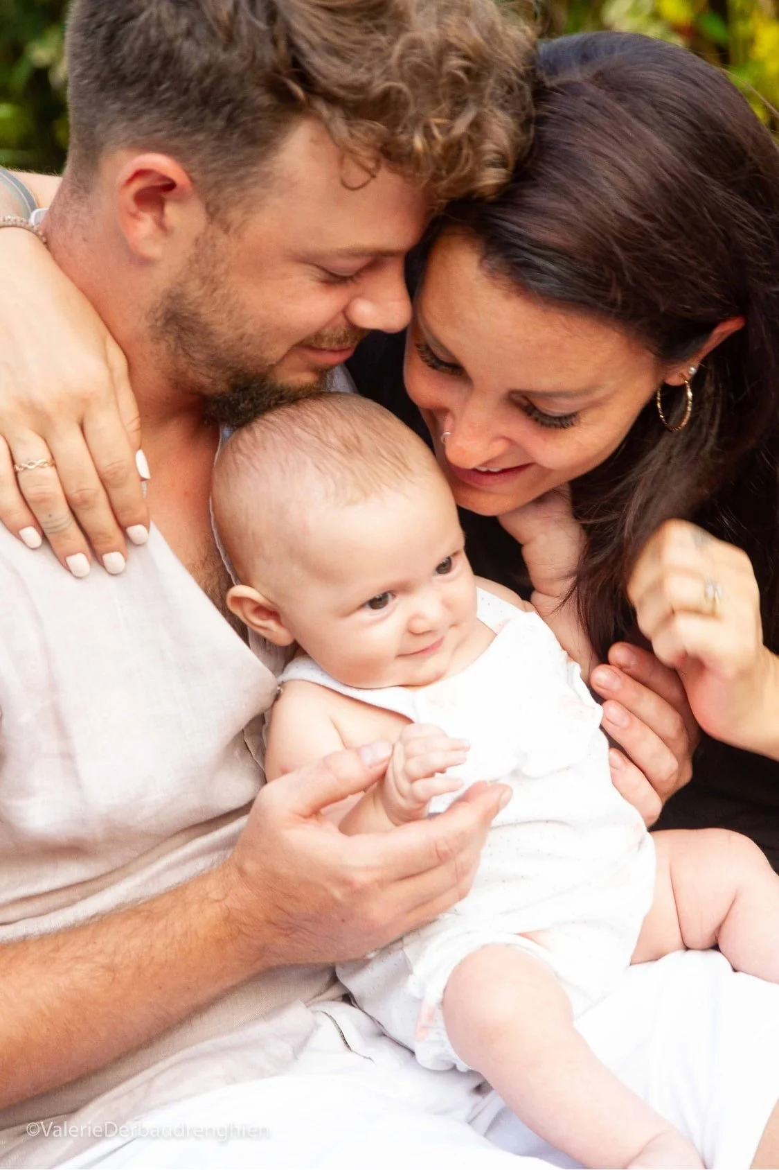 Parents lean in close to their baby in a warm, candid family moment in natural light