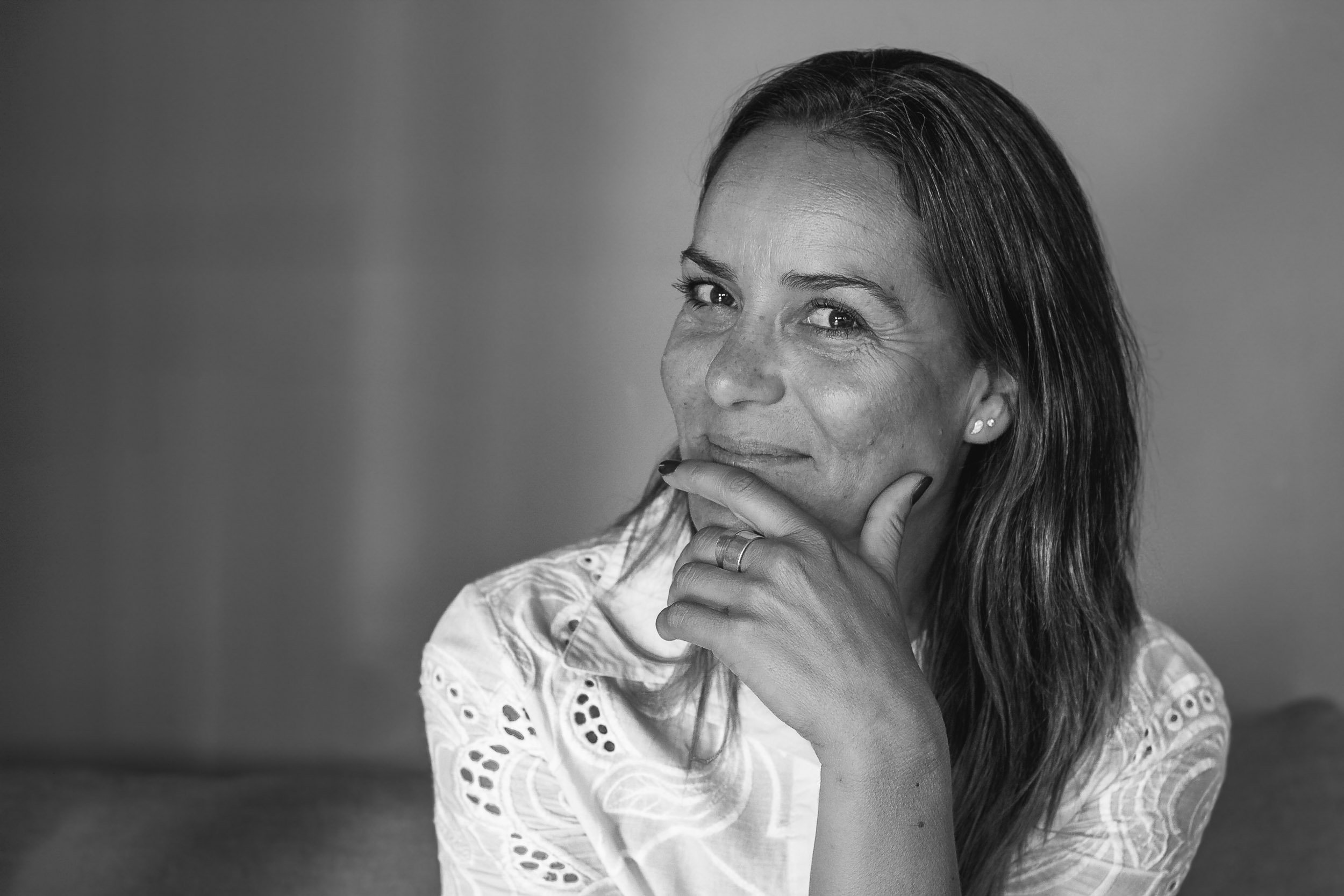 Black and white portrait of a smiling woman resting her hand under her chin in a thoughtful pose.