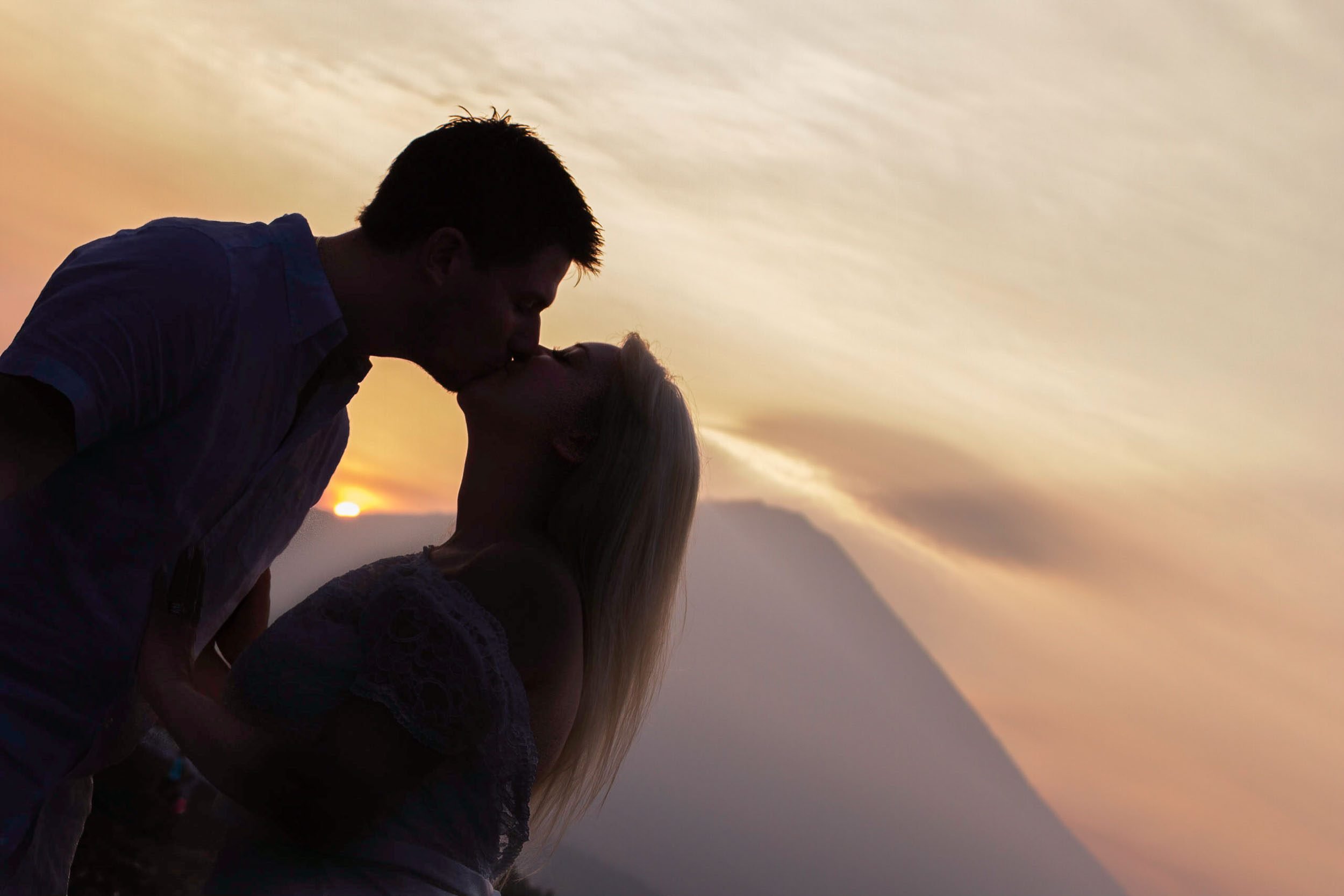 Romantic silhouette profile of a couple kissing against a golden sunset sky with Mount Agung in the background, photographed by Seña Studio.