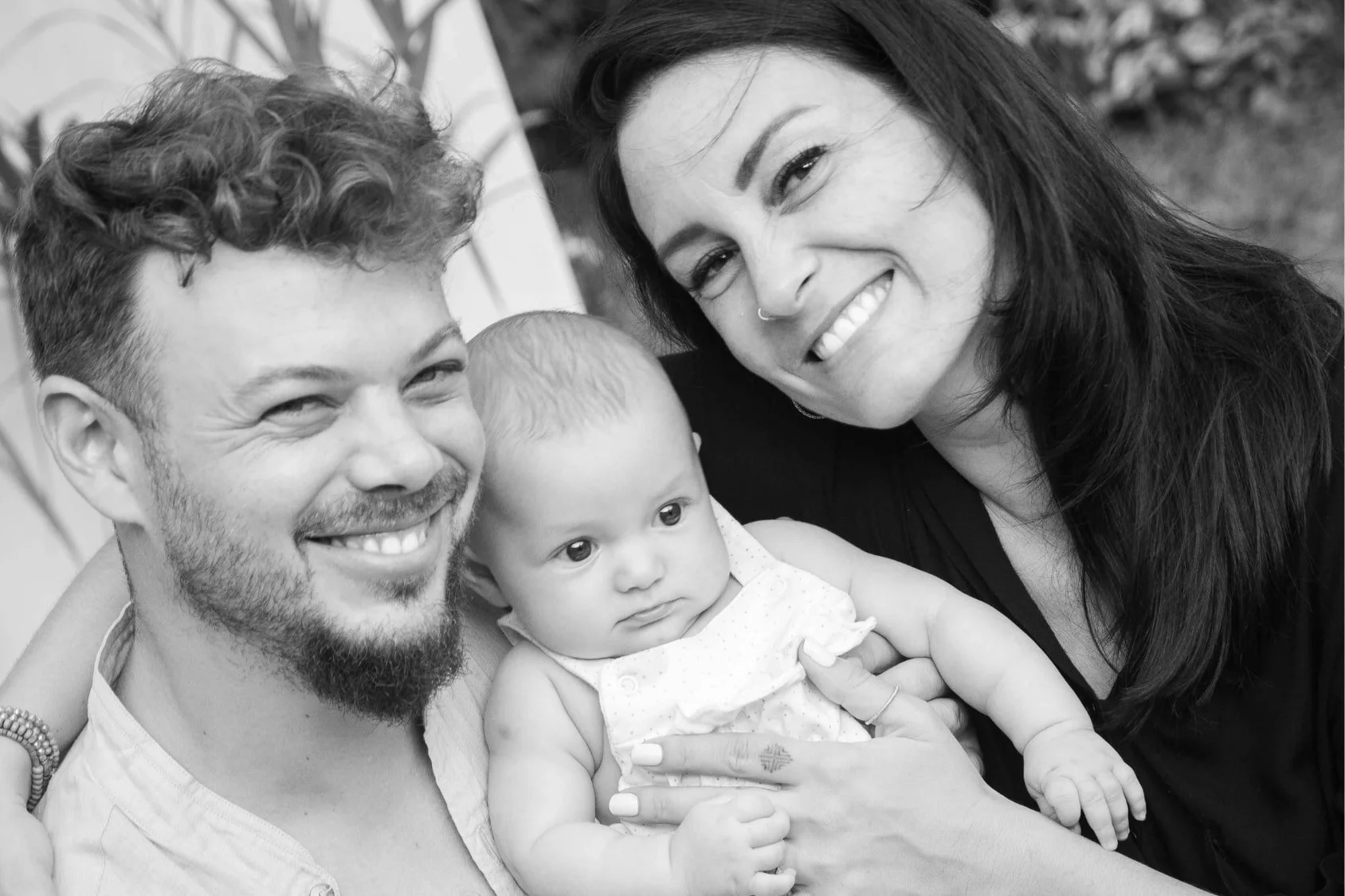 Black and white family portrait of laughing parents holding their baby close