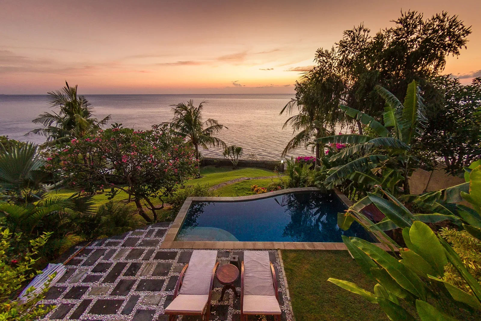High-angle sunset view of a private pool and sun loungers framed by tropical palm trees overlooking the ocean at Aquamarine Beach Villas in Amed, Bali, photographed by Seña Studio.