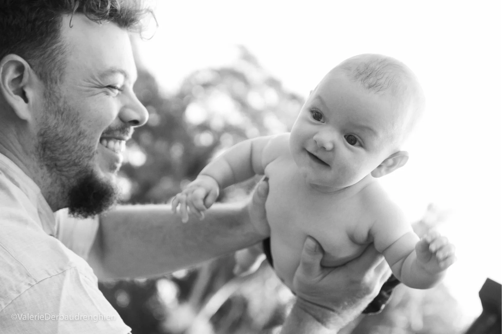 Laughing father lifts his baby into the air, a joyful black and white family photo