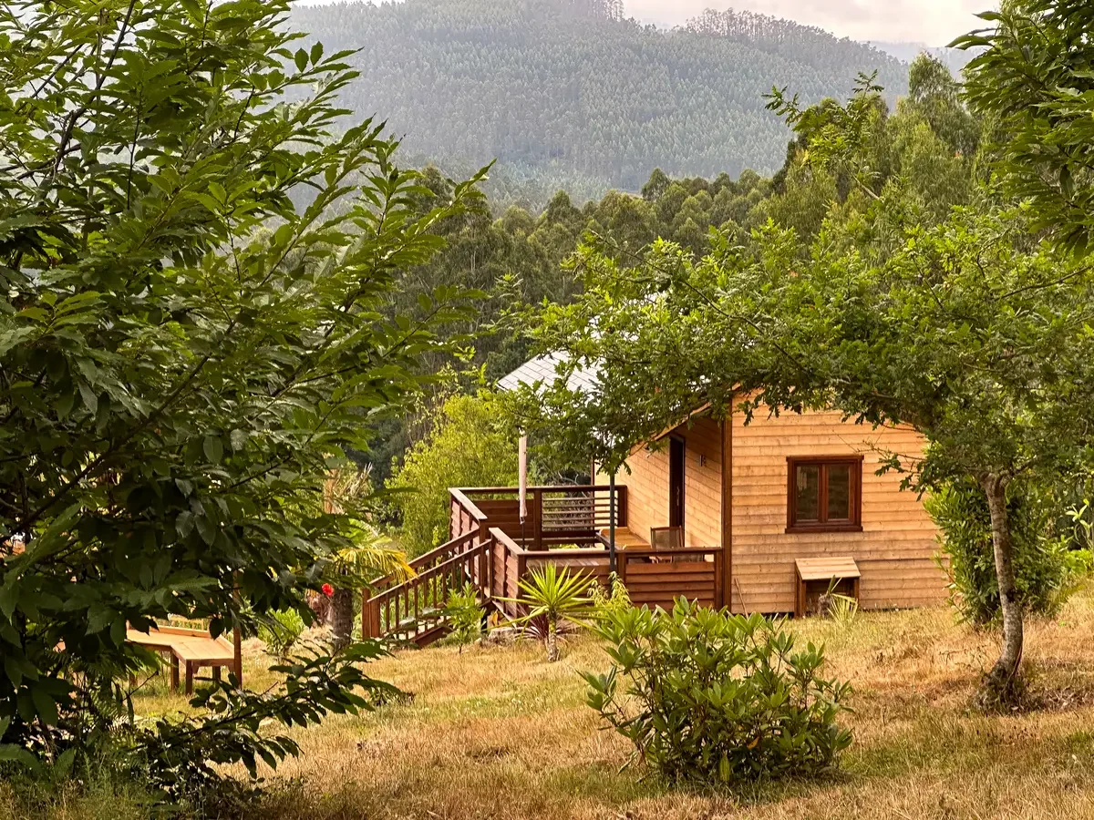 Exterior view of a cozy wooden cabin surrounded by green trees and hills. Haras de Bordo, Galicia.