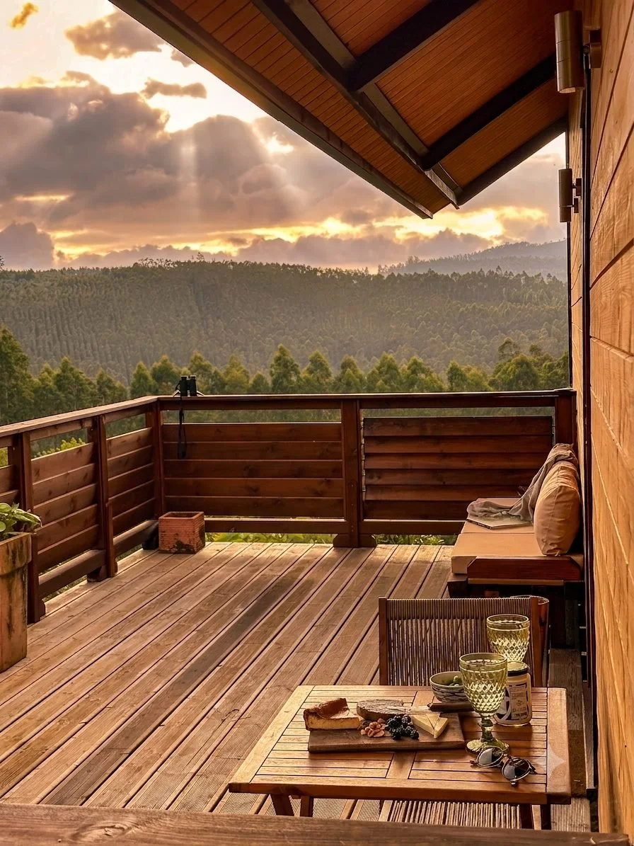 Wooden cabin deck set with drinks and snacks overlooking a misty forest valley under a dramatic sunset with sunbeams at Haras de Bordo, photographed by Seña Studio.