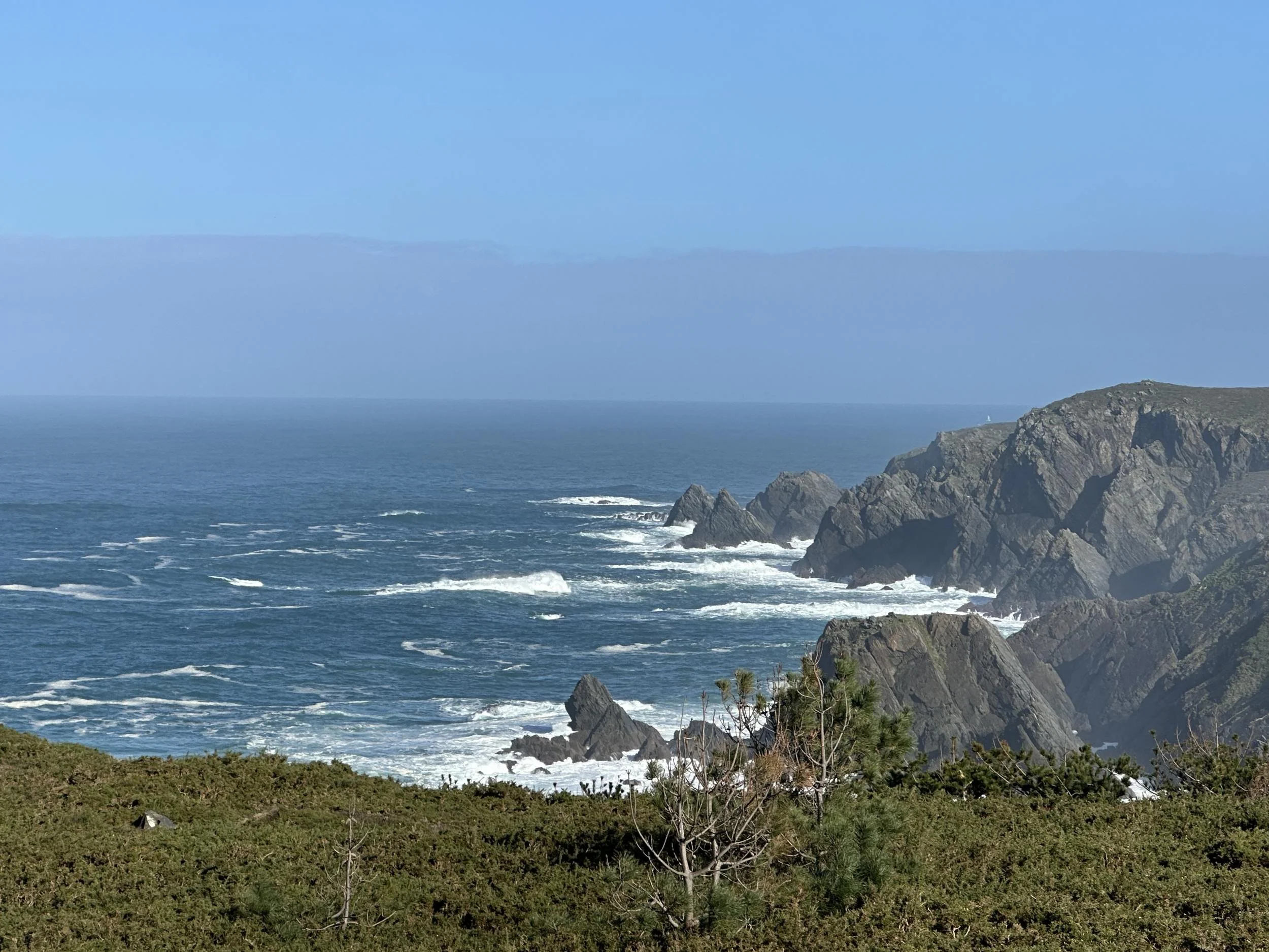 Panoramic view of dramatic rocky cliffs and jagged sea stacks with crashing ocean waves along the wild coast near Pantin Beach, Galicia, photographed by Seña Studio.