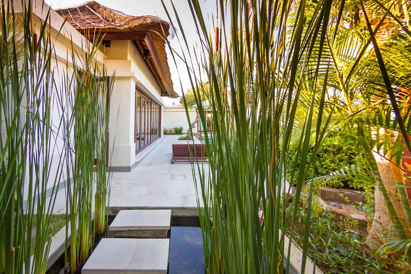 Stone stepping-stone path over a serene koi pond lined with tall reeds outside a luxury villa at The Griya Villas & Spa in Amed, Bali, photographed by Seña Studio.