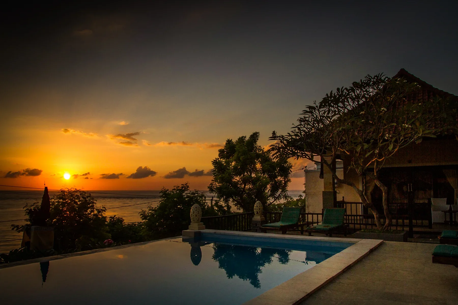 Sunset over an oceanfront villa infinity pool with palm trees and lounge chairs in Amed, Bali, photographed by Seña Studio.