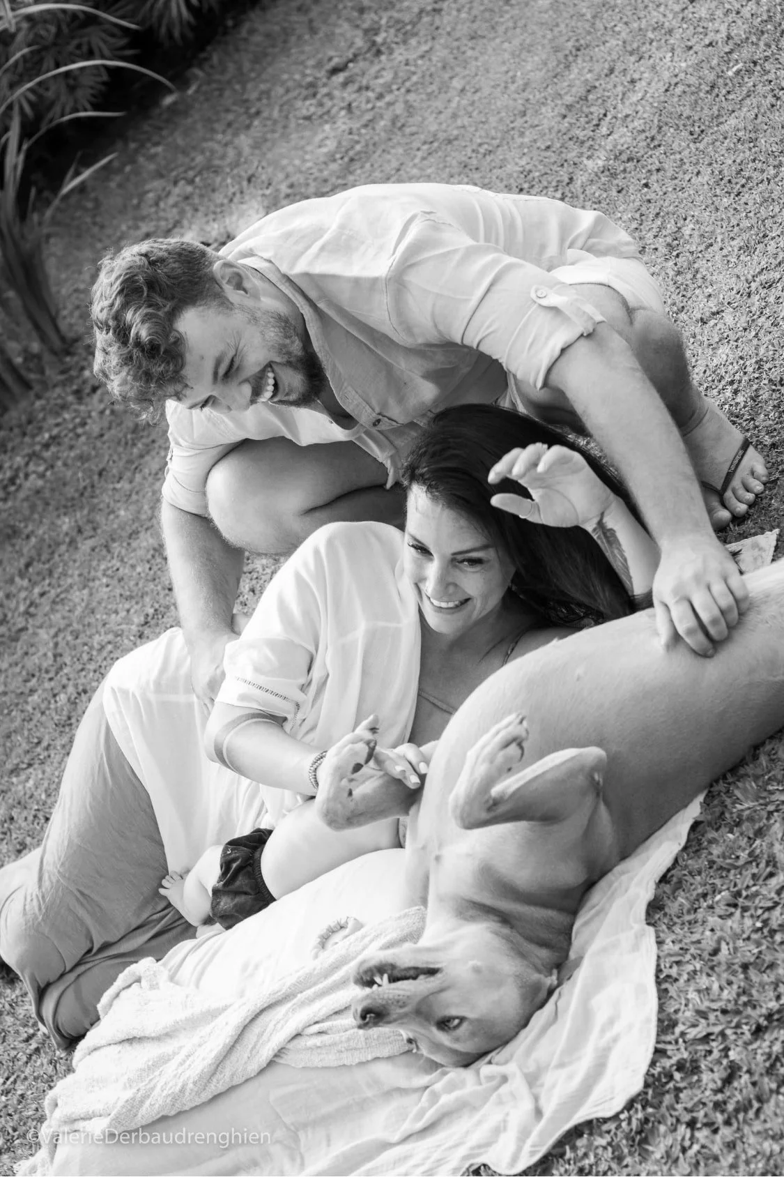 Parents laugh with their dog on a picnic blanket, candid black and white family photography