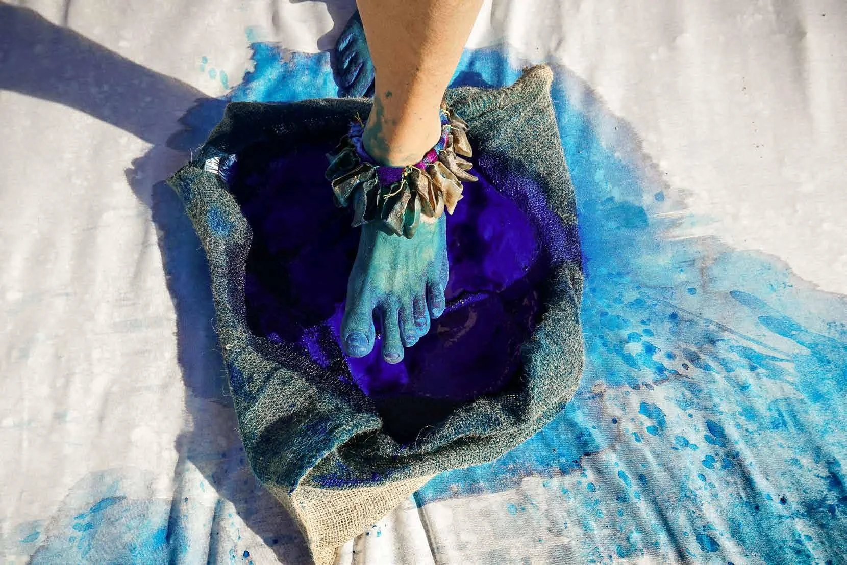 A person's foot is dipped in blue paint and is standing on a cloth, with some paint splattered around.
