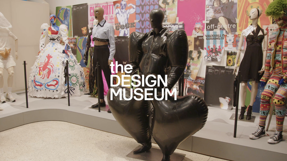 Display of various mannequins dressed in colorful and eclectic outfits at The Design Museum, with vibrant posters and fashion-themed artworks in the background.